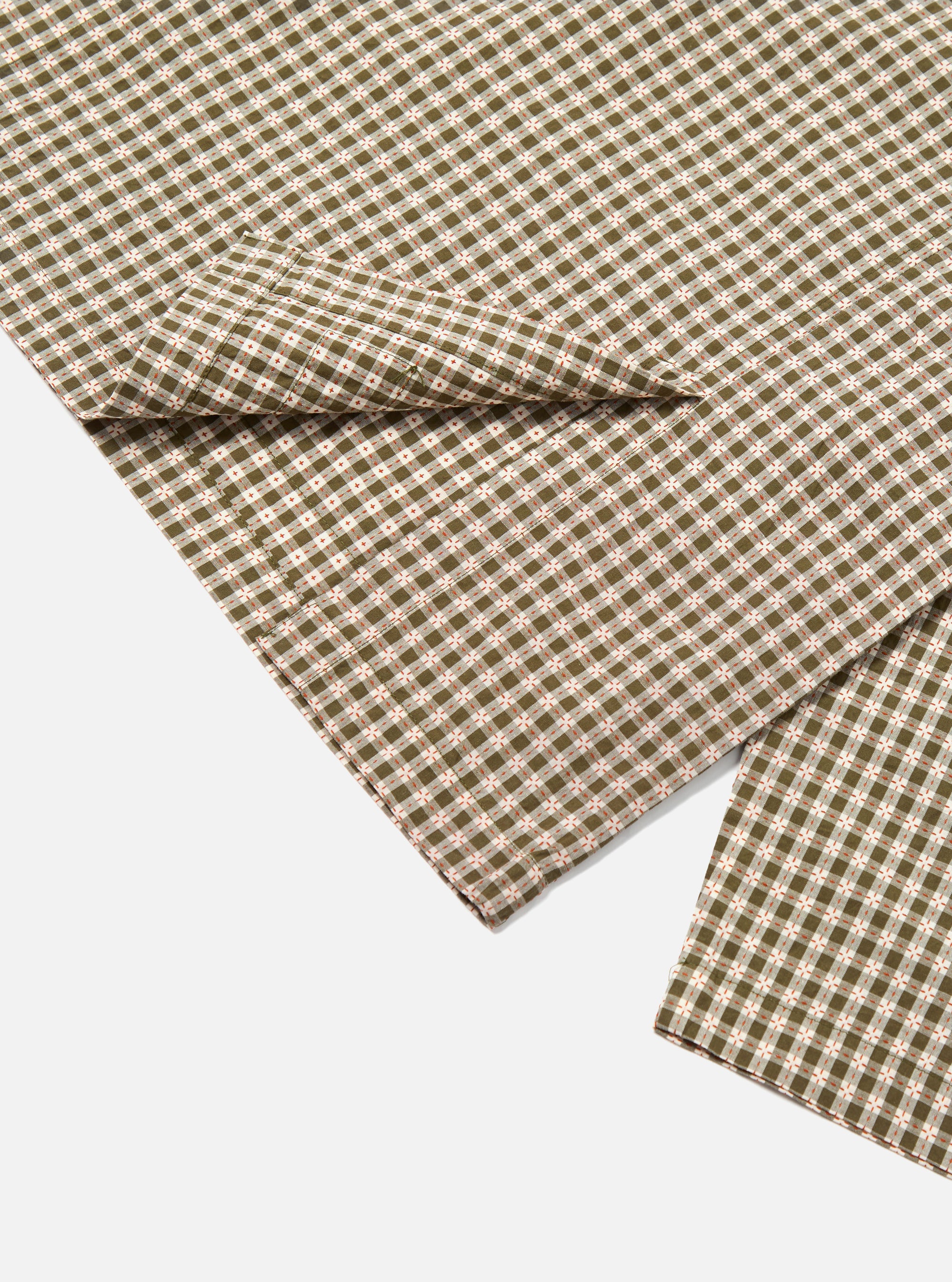 Close-up of the Olive Dobby Check Cancun Jacket fabric. The jacket has a green and white check pattern with red accents, laid on a white surface.
