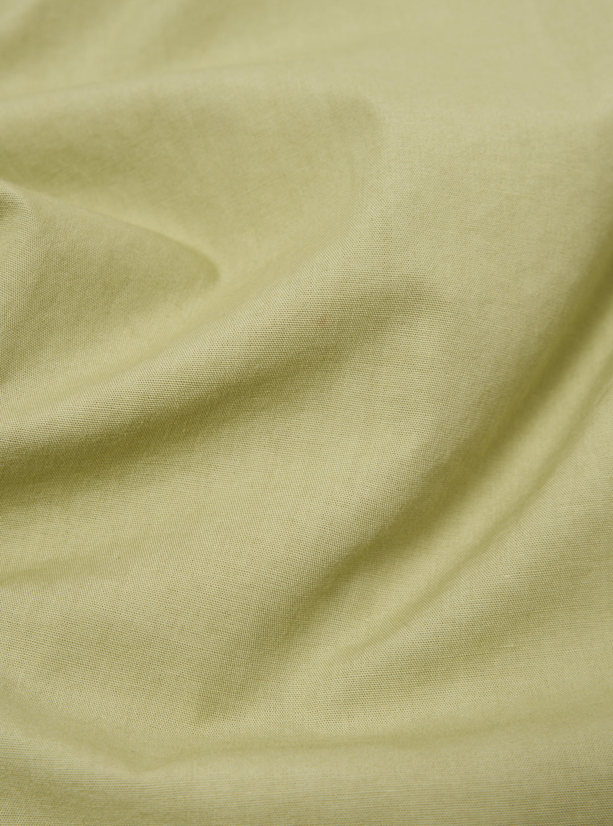 Close-up of the pale green broadcloth fabric of the Cancun Jacket, showing its texture and color. The jacket is draped on a flat surface.