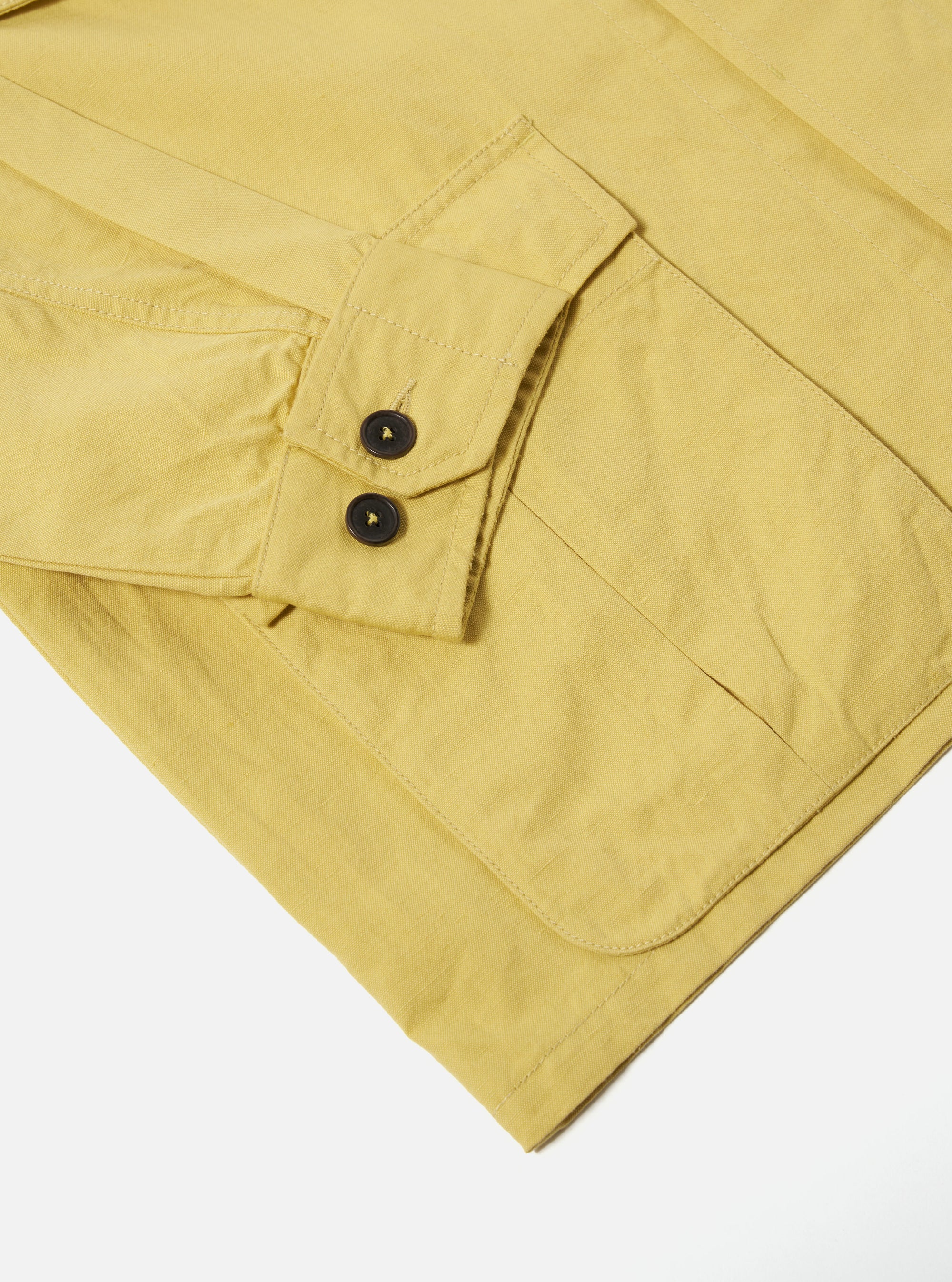 Close-up of the lemon-colored Linen Slub Weave Jungle Jacket on a white surface. Shows the sleeve with buttons and pocket detail.