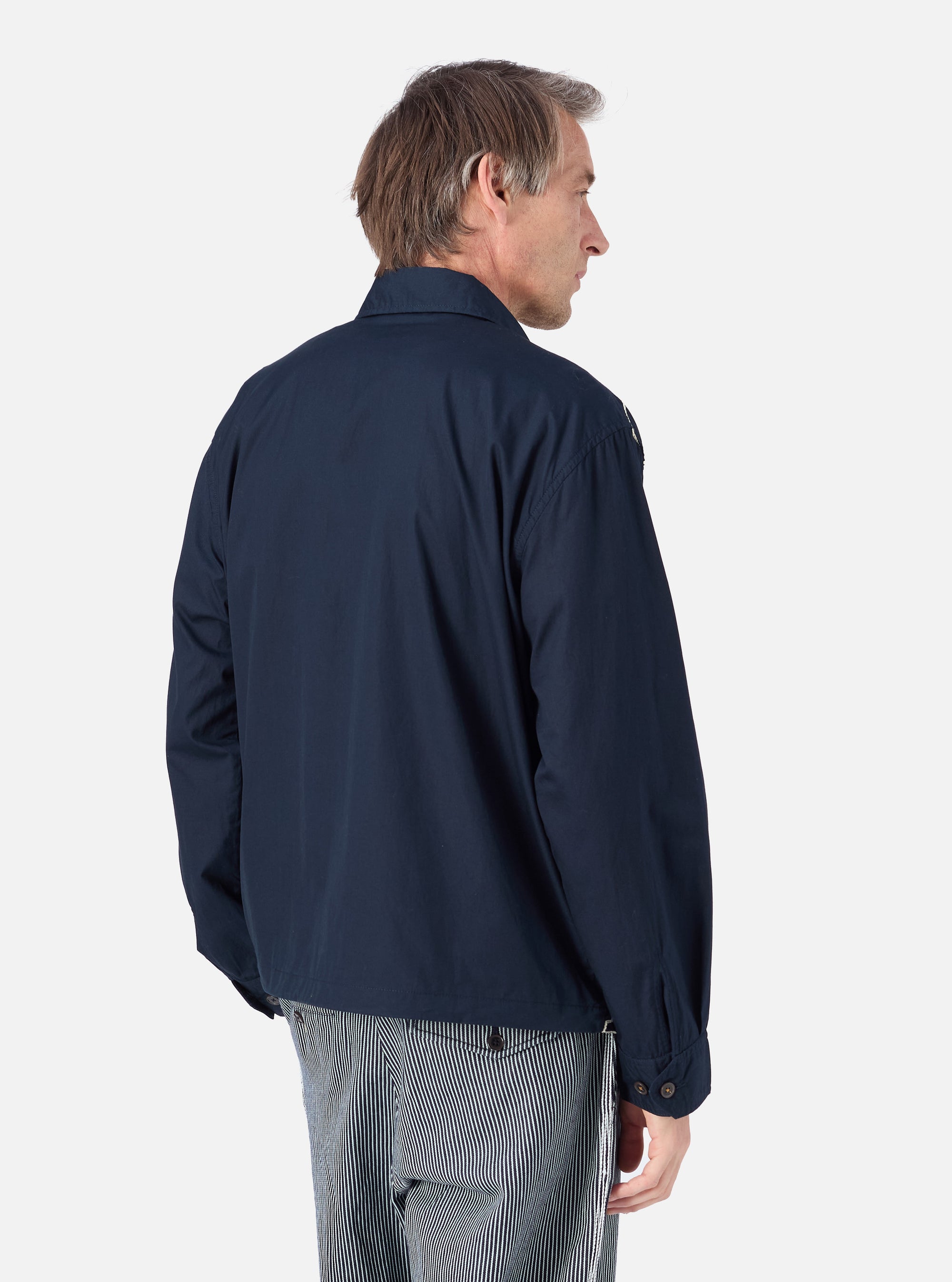 A man in profile wears the Navy Mitla Broadcloth Club Jacket against a white background. The jacket is a dark navy color. He also wears striped pants.