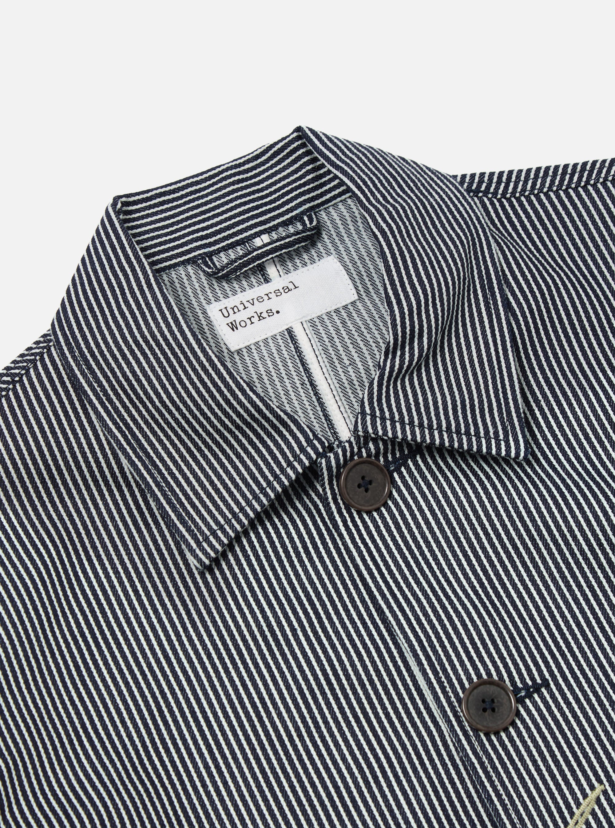 Close-up of the Indigo Hickory Stripe Denim Original Bakers Jacket. Features a blue and white striped pattern, button closure, and a classic collar. Shot on a white background.