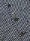 Close-up of the Indigo Hickory Stripe Denim Original Bakers Jacket. Features include brown buttons, a striped pattern, and denim material. Shot on a flat surface.