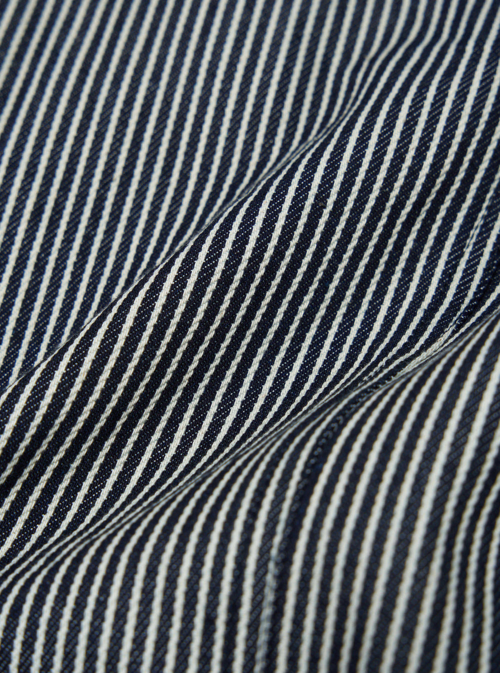 Close-up of the Indigo Hickory Stripe Denim Original Bakers Jacket. The image shows the texture and pattern of the blue and white striped denim fabric.