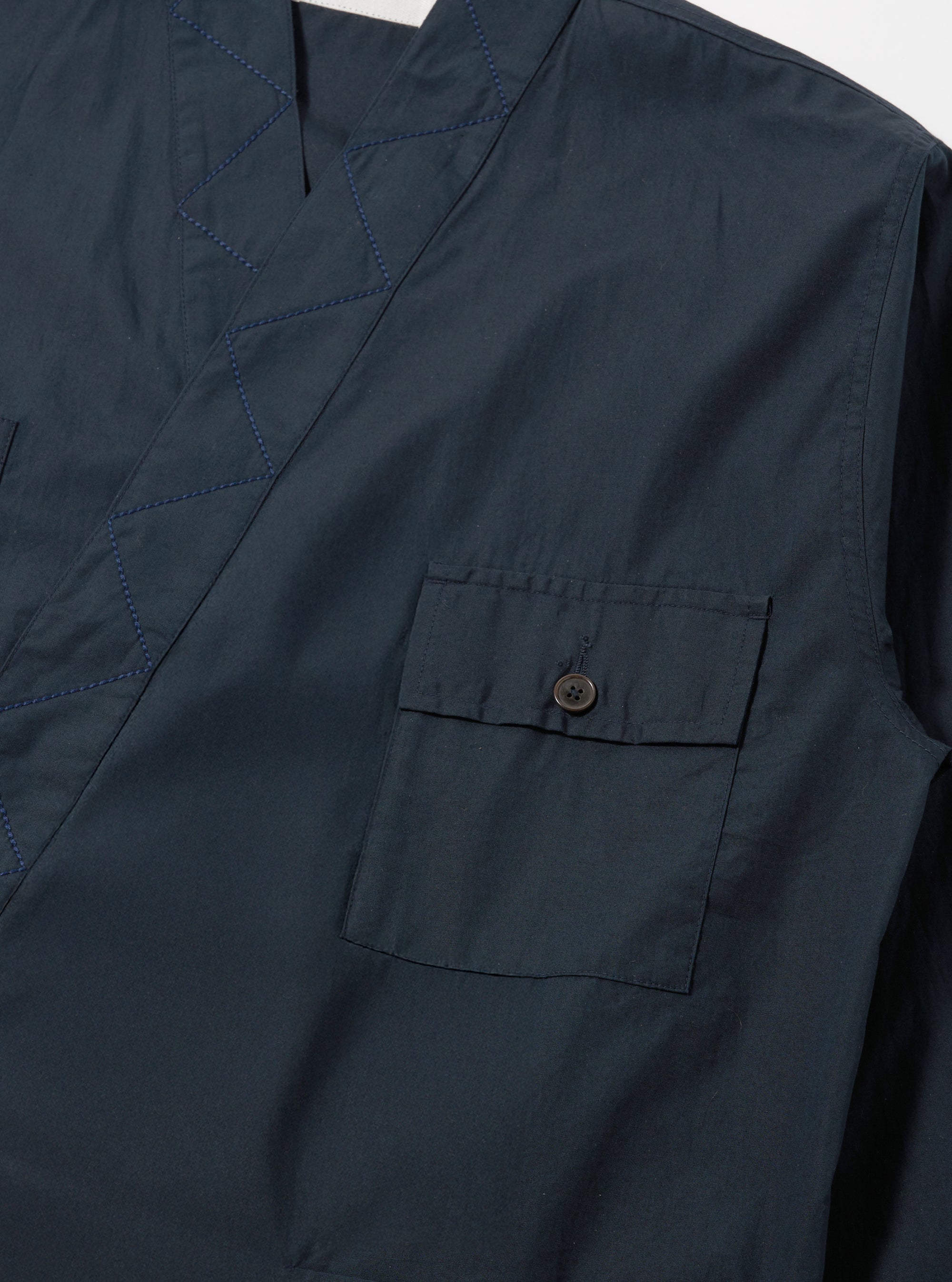 Close-up of the Navy Broadcloth Osaka Work Jacket in navy broadcloth. Features a chest pocket with button closure and blue stitched detailing. Shot on a flat, neutral surface.