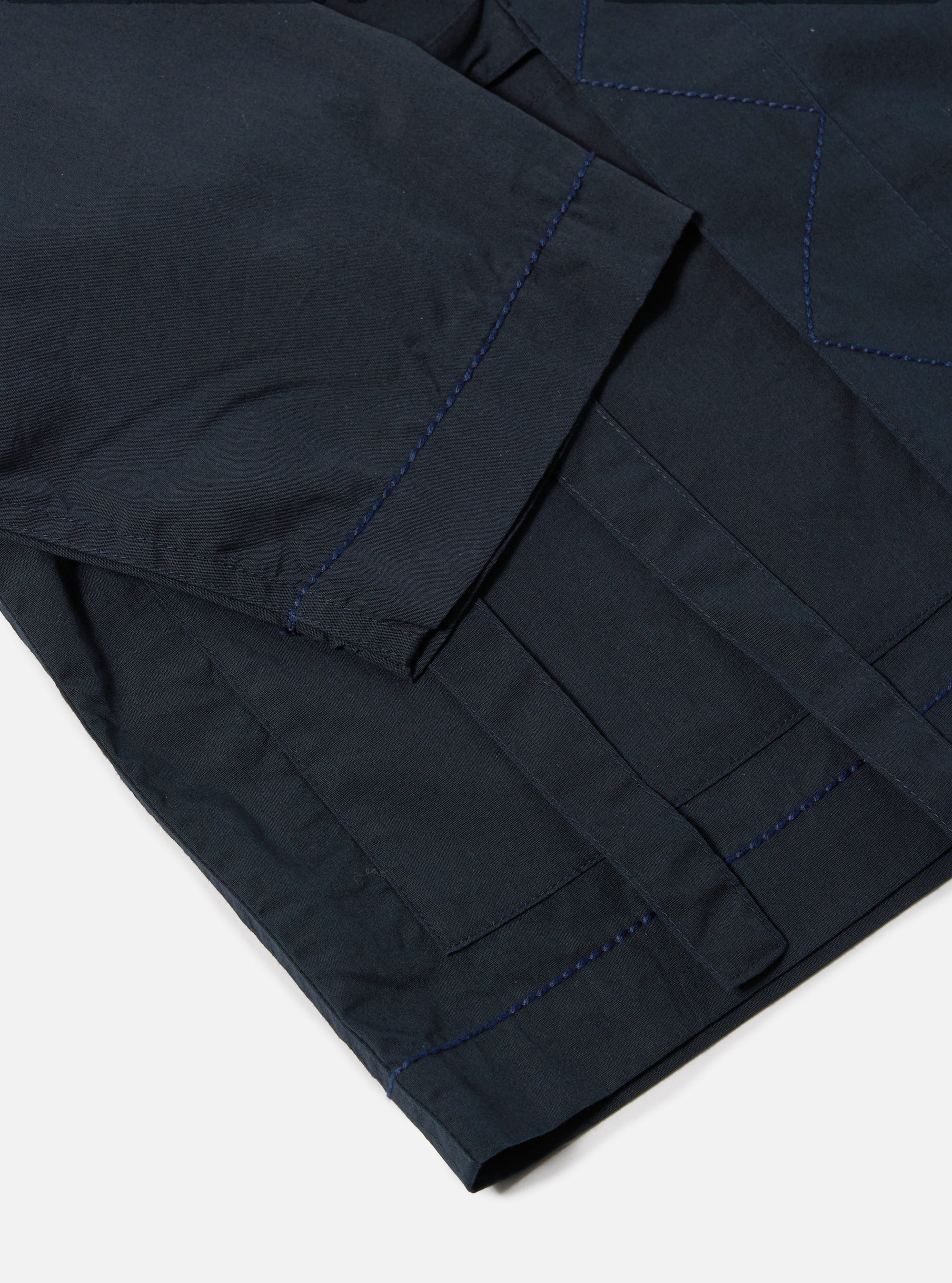 Close-up of the navy broadcloth Osaka work jacket on a white surface. Shows the jacket's pocket and stitching details.