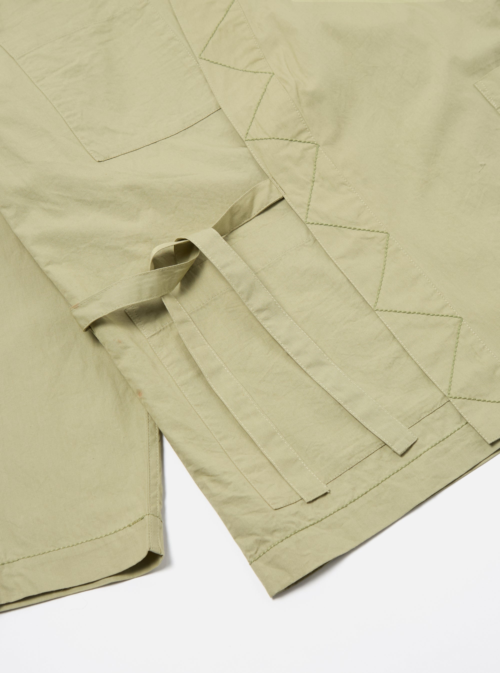 Close-up of the pale green Broadcloth Osaka Work Jacket on a white surface. Details include pockets, belt loops, and decorative stitching.
