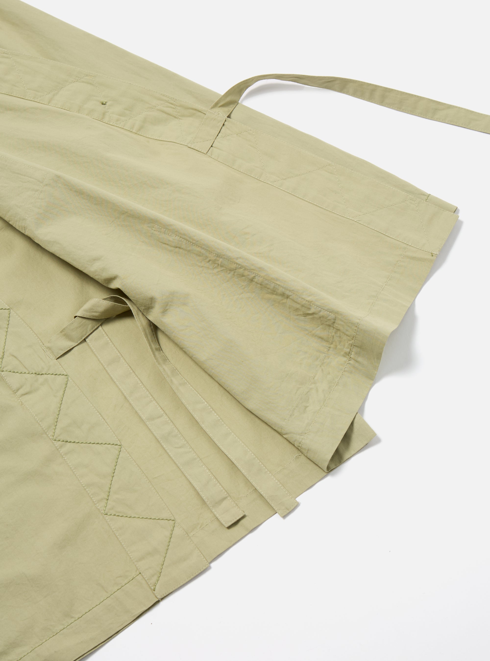 Close-up of the pale green Broadcloth Osaka Work Jacket on a white surface. The jacket features a tie closure and geometric stitching details.