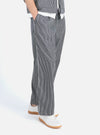 A person wears the Indigo Hickory Stripe Denim Duke Pant in a studio shot. The pants are blue and white striped denim. The background is a bright white.