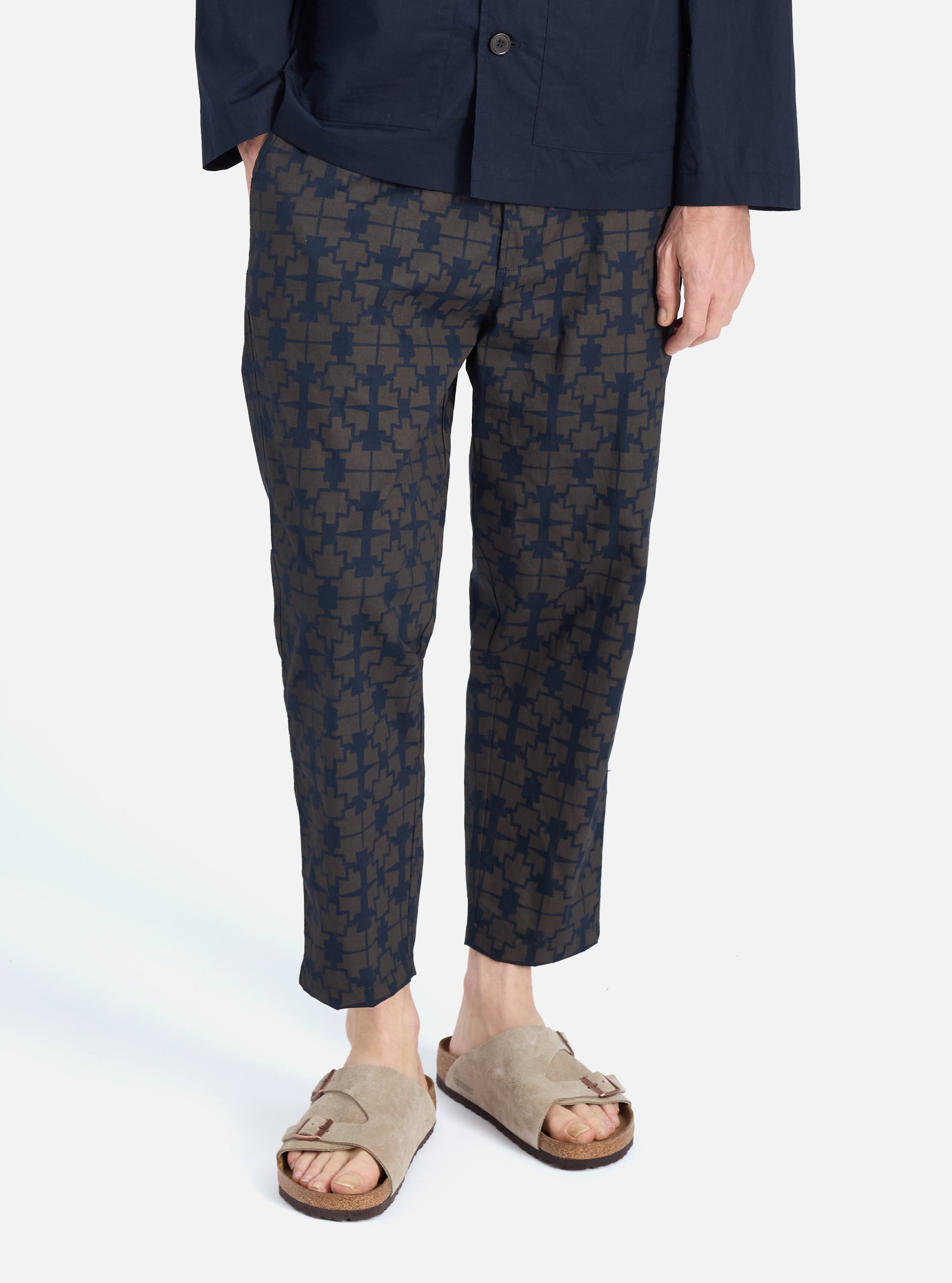 A man models the Navy Mitla Print Cotton Hi Water Trouser against a white background. The trousers feature a navy and brown geometric print and a cropped fit.
