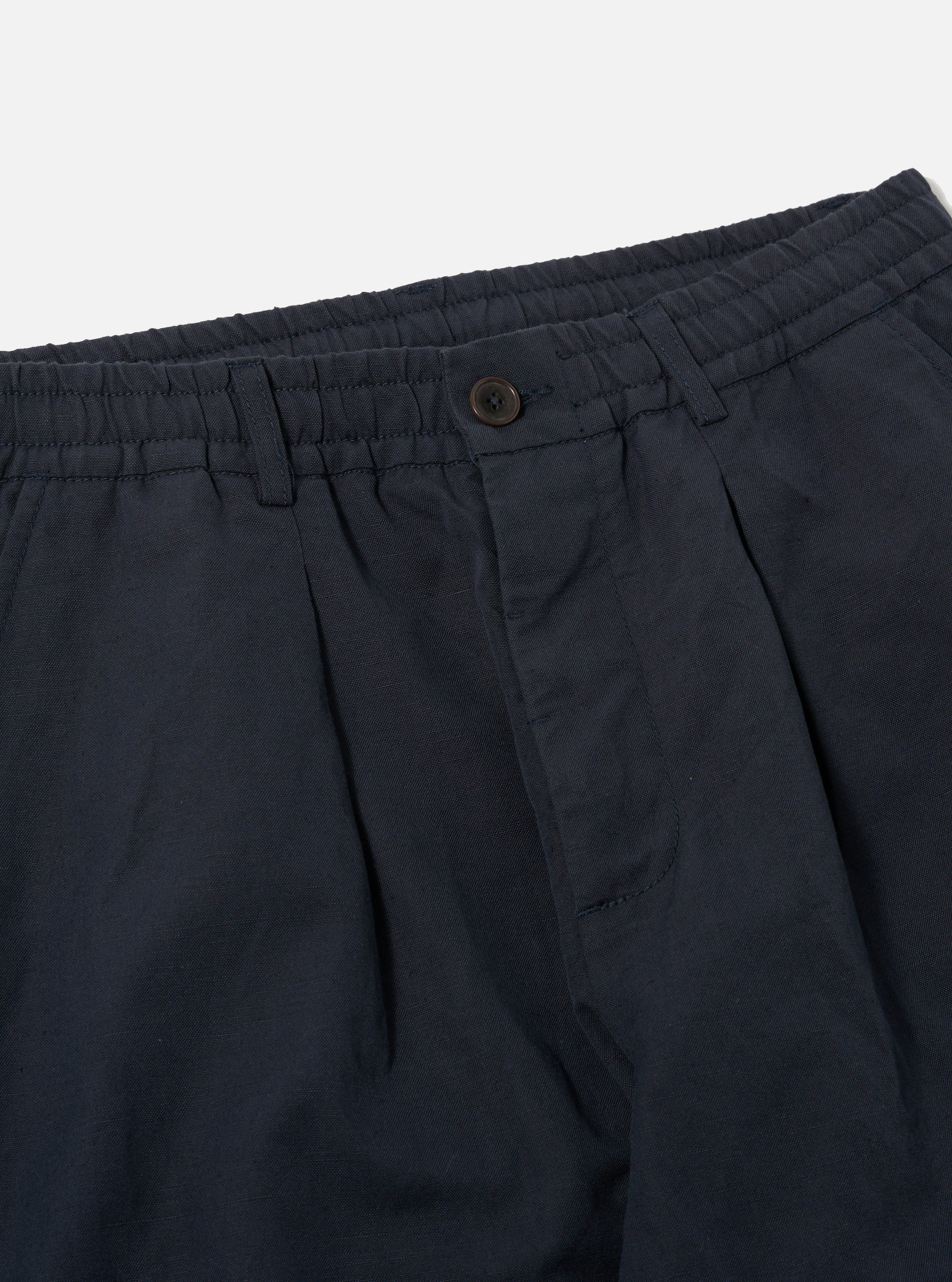 Close-up of the Navy Linen Slub Weave Oxford Pant on a white background. Shows the navy color, linen texture, button closure, and pleated design.