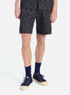 A man stands on a white background wearing the Navy Mitla Print Cotton Simple Short. The shorts have a navy and brown pattern. He also wears navy socks and sneakers.