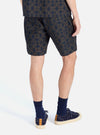 A man stands against a white backdrop, showcasing the Navy Mitla Print Cotton Simple Short. The shorts feature a navy and brown pattern. He wears navy socks and matching sneakers.