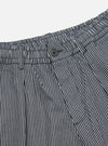 Close-up of the Indigo Hickory Stripe Denim Pleated Track Short. The denim is striped with white and indigo. Features a button closure and pleated design.