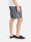 Side view of a model wearing Indigo Hickory Stripe Denim Pleated Track Short on a white background. The denim shorts have a pleated design and a relaxed fit.