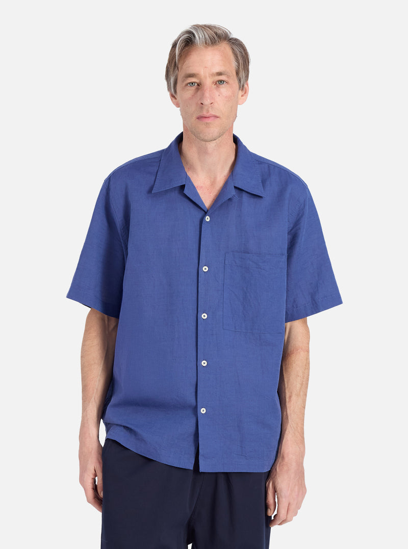 A model poses in a Blue Linen Cotton Shirting Camp Shirt against a white backdrop. The shirt is a relaxed fit, made from a breathable linen-cotton blend.