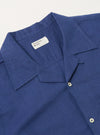 Close-up of the Blue Linen Cotton Shirting Camp Shirt. The blue linen-cotton blend is visible, along with the camp collar and button details. Shot on a white surface.
