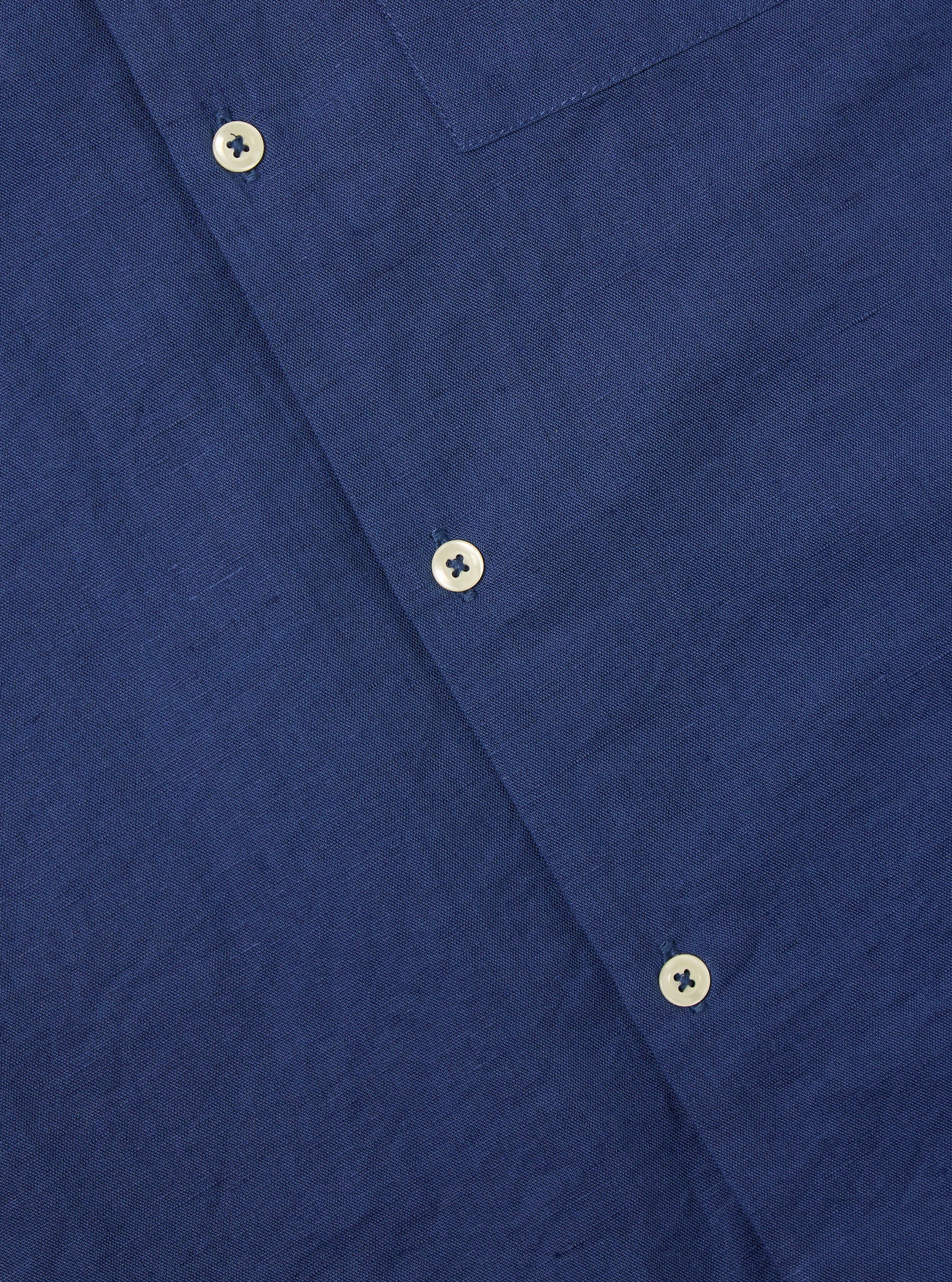 Close-up of the Blue Linen Cotton Shirting Camp Shirt showing the fabric texture and button details. The shirt is laid flat on a neutral surface.