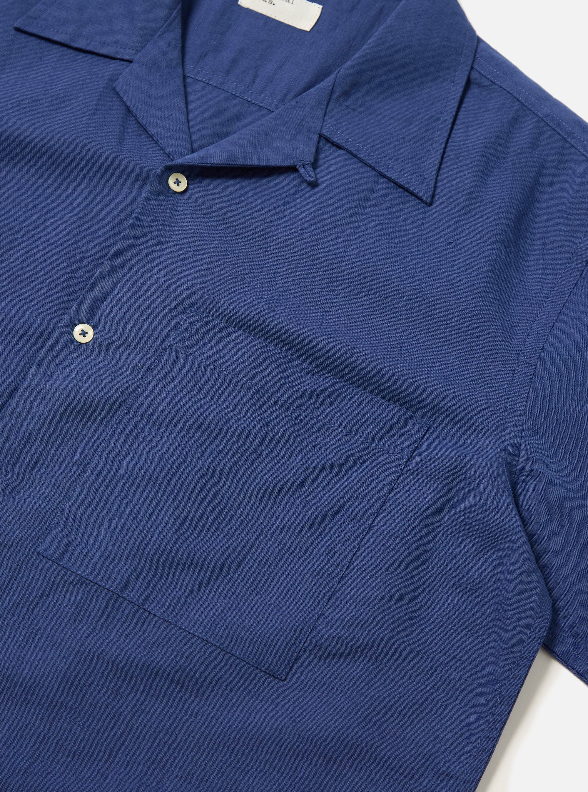 Close-up of the Blue Linen Cotton Shirting Camp Shirt on a white surface. The shirt is a rich blue with a camp collar, chest pocket, and button closure.
