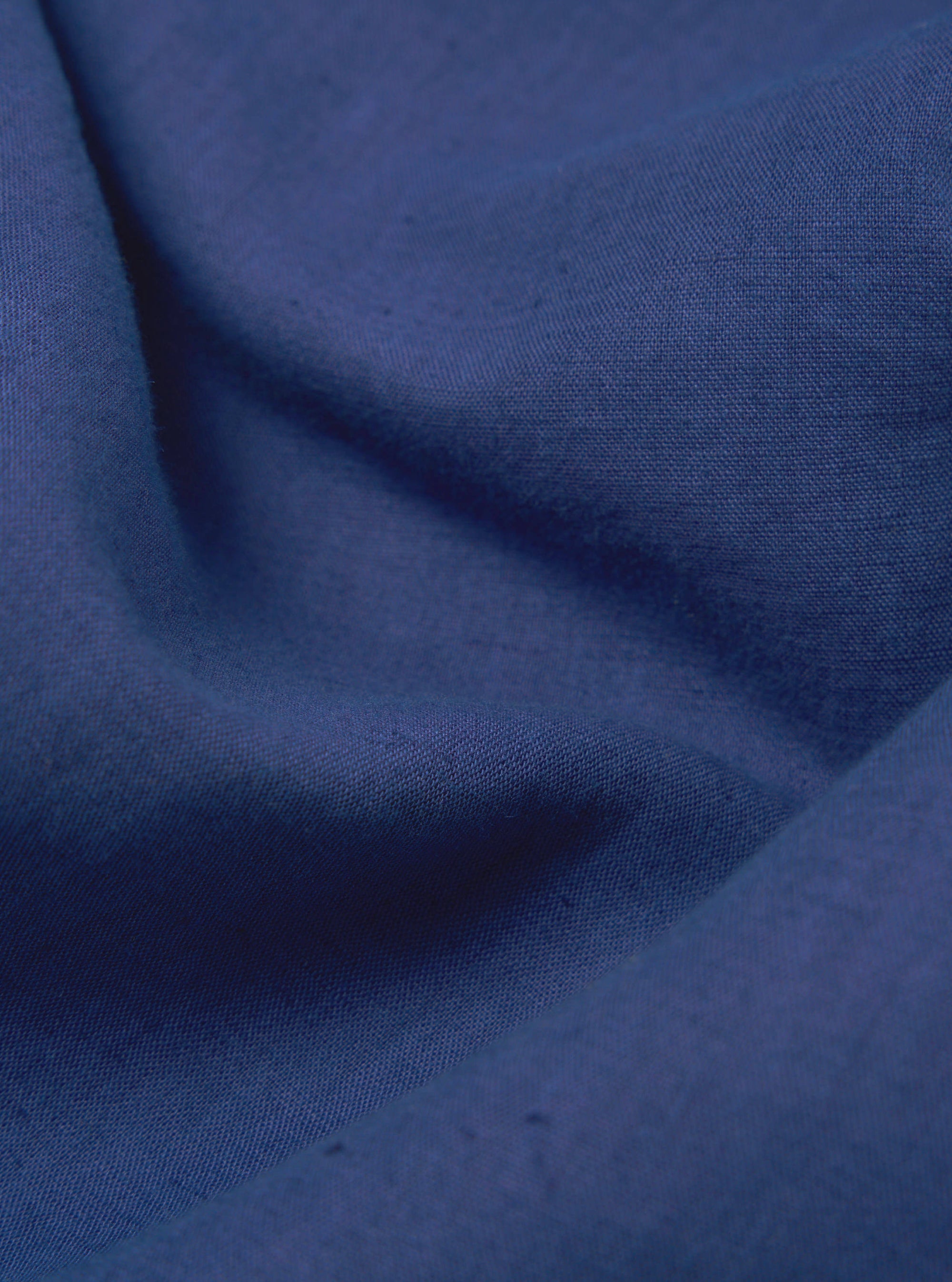 Close-up of the blue linen cotton shirting camp shirt fabric. The material is draped to show texture and color.
