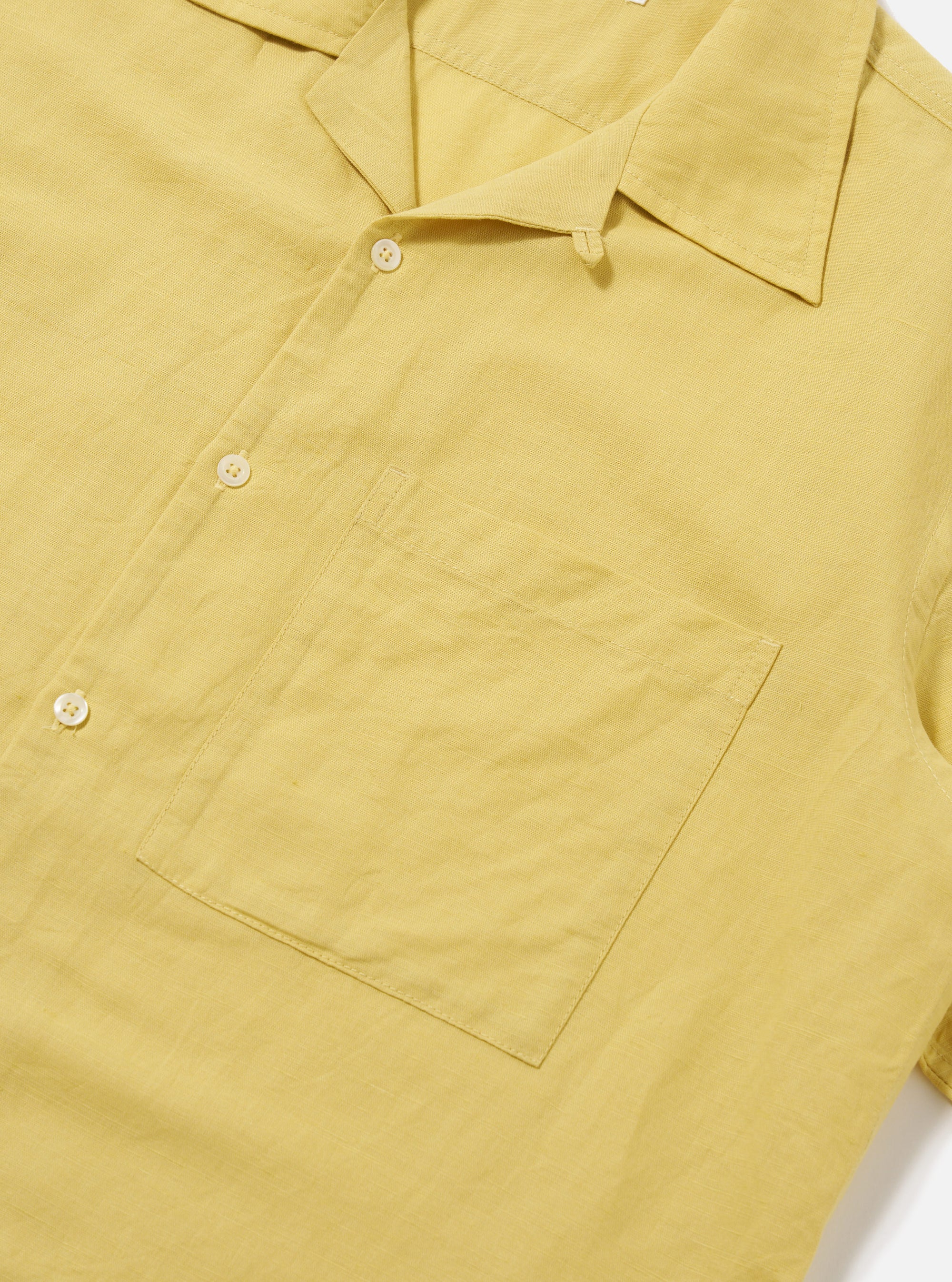 Close-up of the Lemon Linen Cotton Shirting Camp Shirt. The shirt is a light yellow color and has a pocket on the left chest. The background is a plain white.
