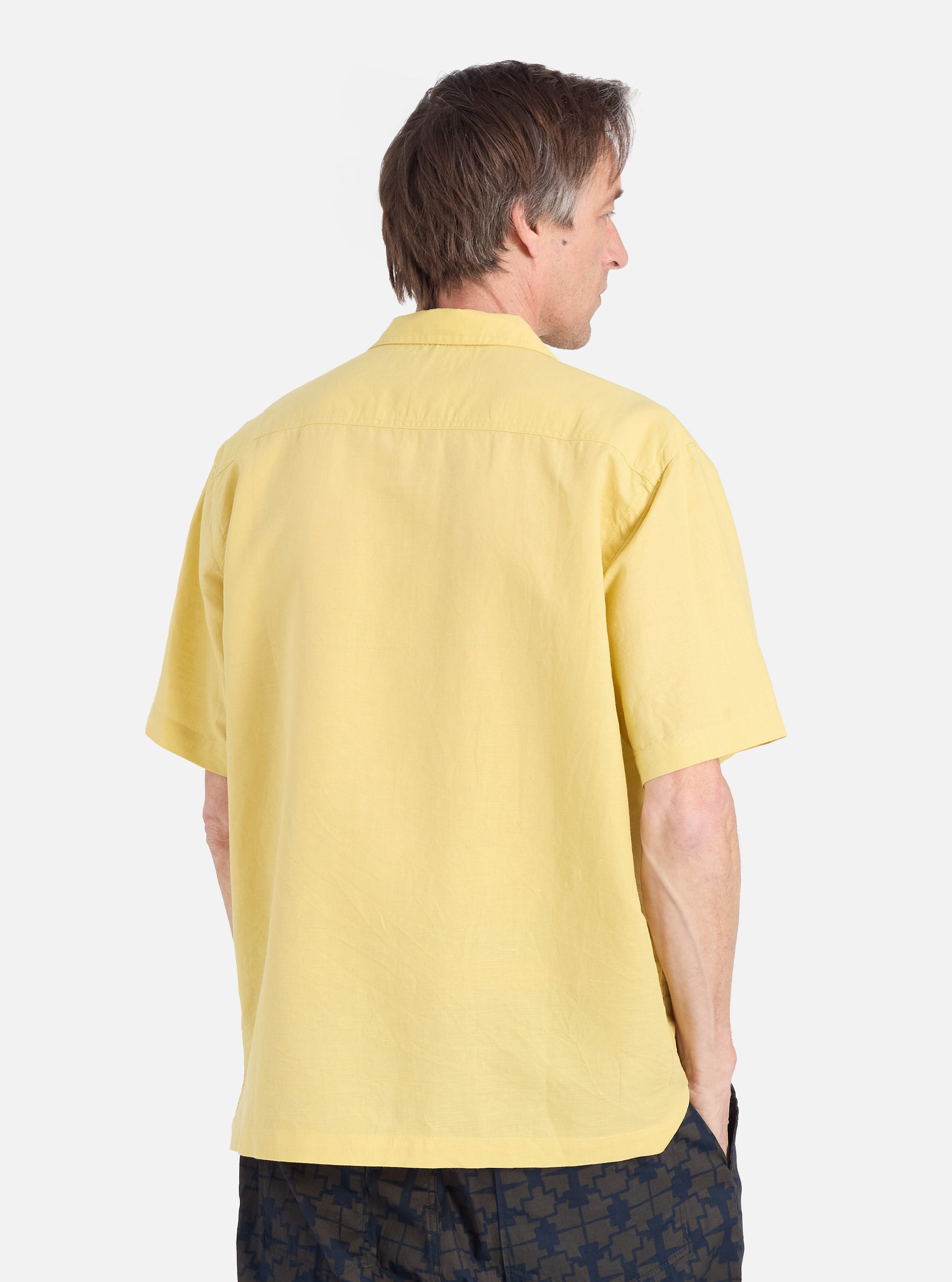 Back view of a man wearing a Lemon Linen Cotton Shirting Camp Shirt. The shirt is a light yellow color and has short sleeves. The background is a plain white.