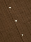 Close-up of the Brown Dobby Self Stripe Camper Shirt. The brown dobby fabric has self stripes. White buttons are visible. Two chest pockets. Shot on a flat surface.