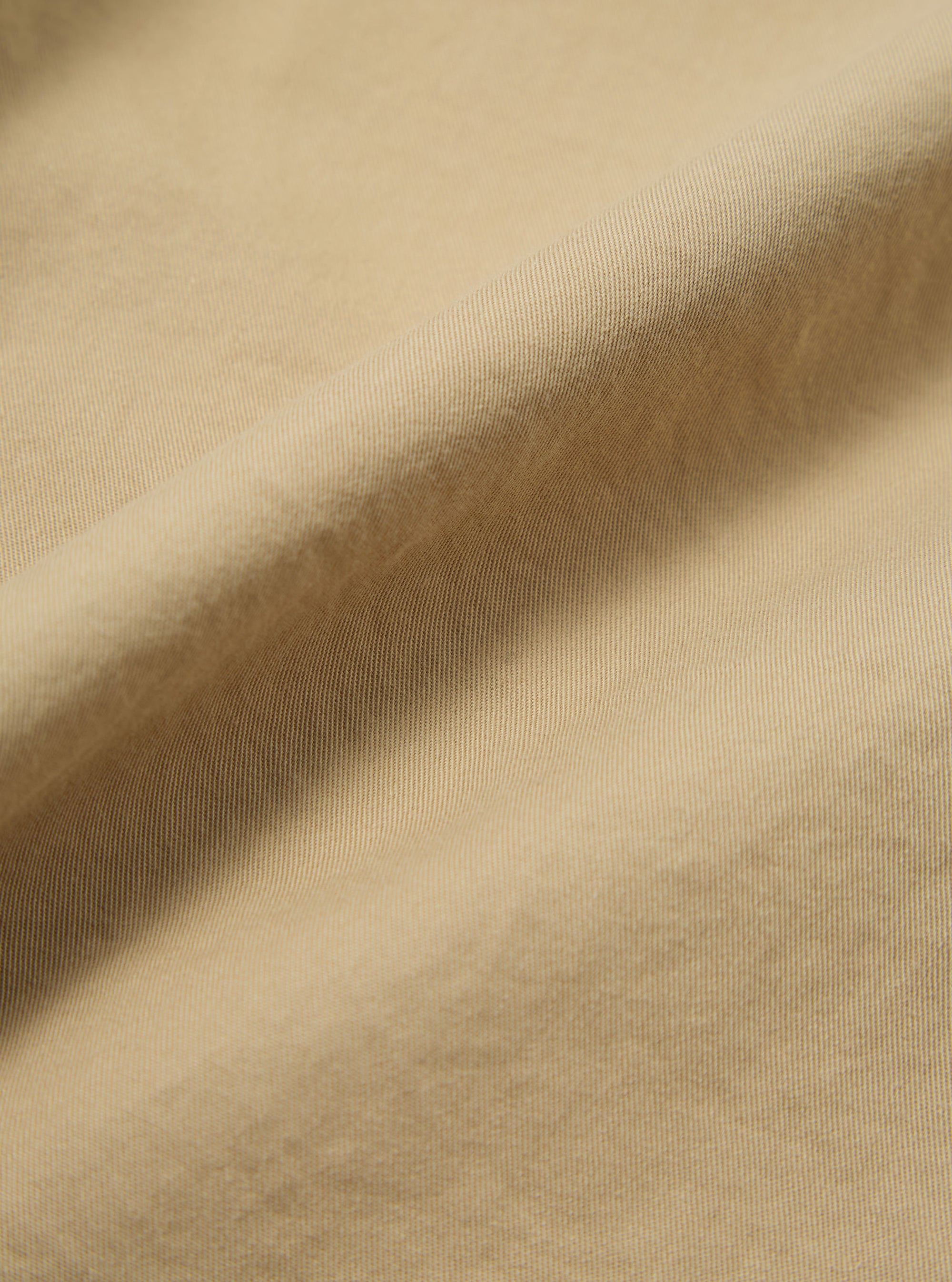 Close-up of the Sand Military Cotton Judo Pant fabric. The sand-colored cotton is draped to show texture. The background is a plain surface.