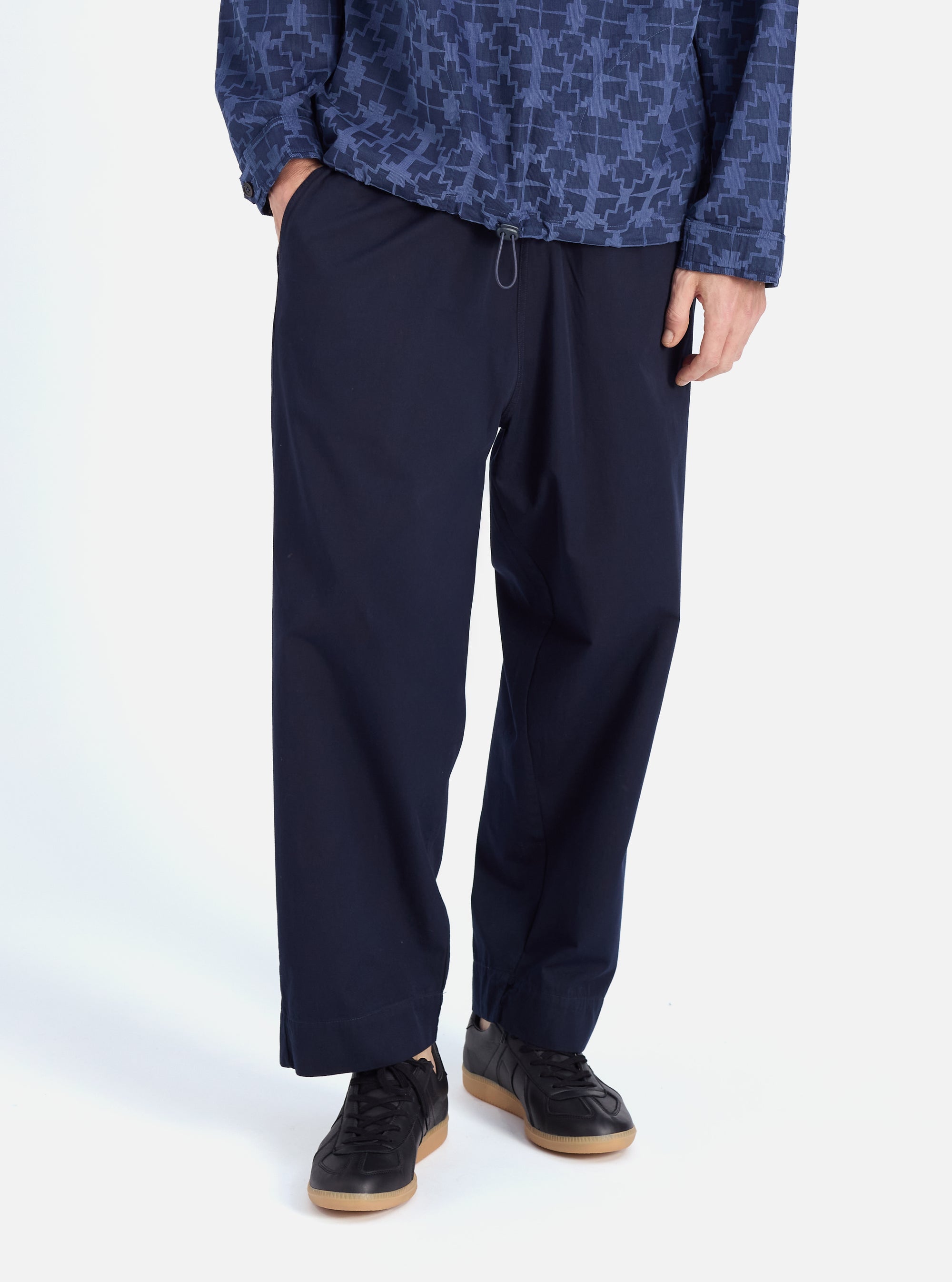 Model wears Navy Military Cotton Judo Pant in studio. These loose-fitting, navy cotton pants are paired with black sneakers. The background is a clean white.