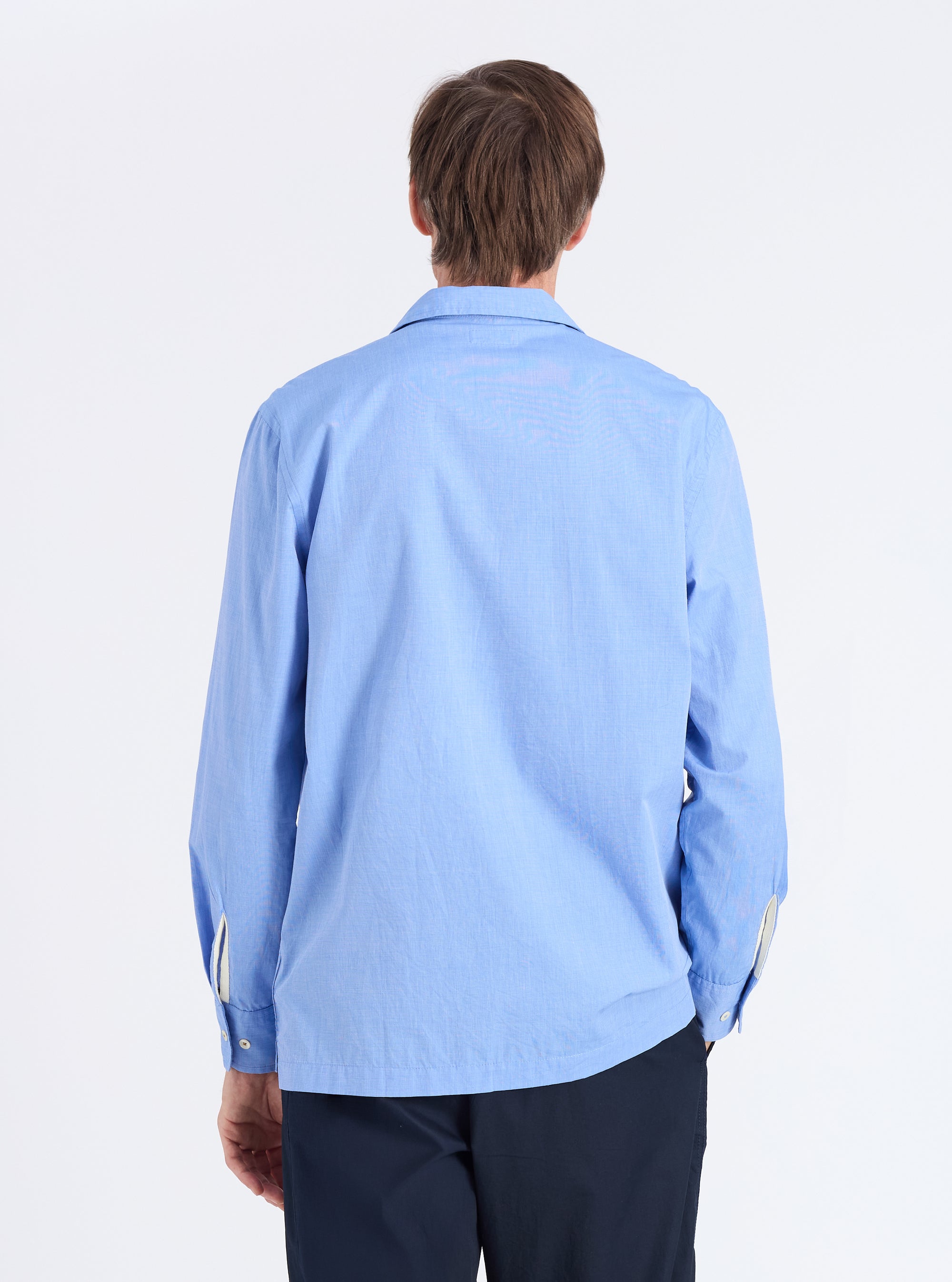Back view of a man wearing a Blue End On End Cotton Garage Shirt. The light blue shirt is paired with dark pants, against a white backdrop.