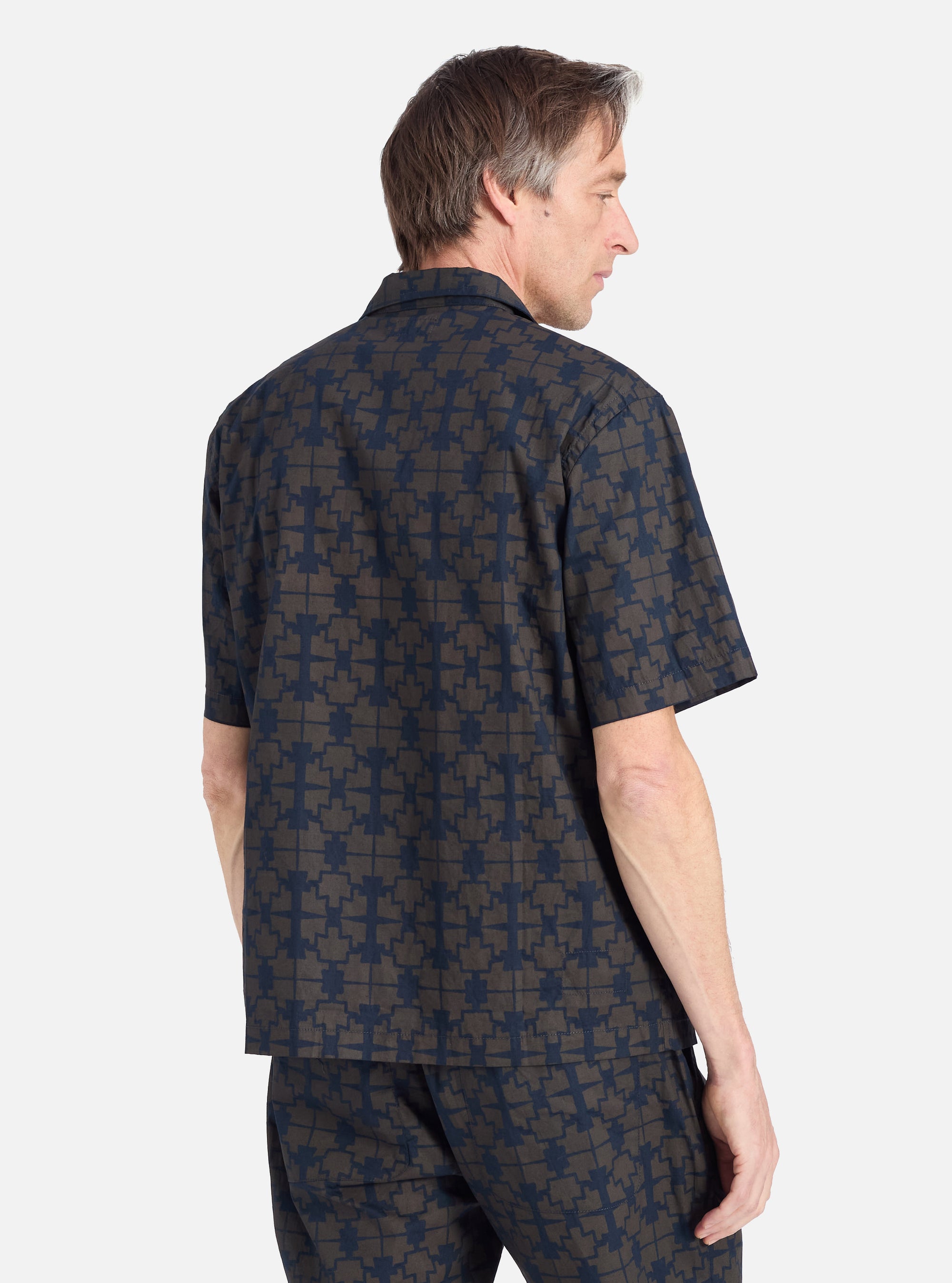 A man wears the Navy Mitla Print Cotton Road Shirt, a short-sleeved button-down with a geometric pattern. Shot in a studio against a white backdrop.