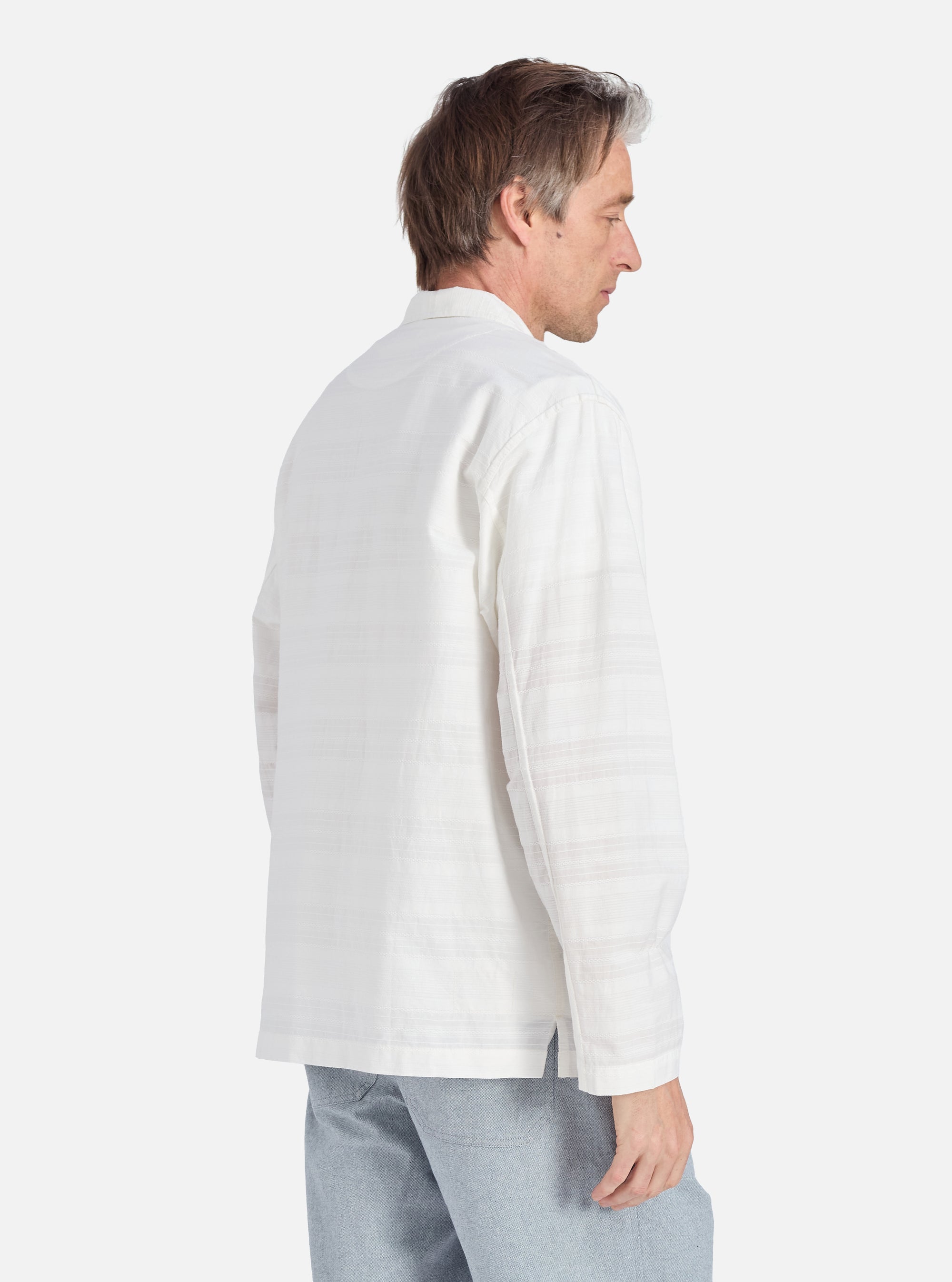 A man on a white background models the Ecru Deffe Self Stripe Smock Overshirt. The shirt is a light ecru color with subtle stripes and a relaxed fit.