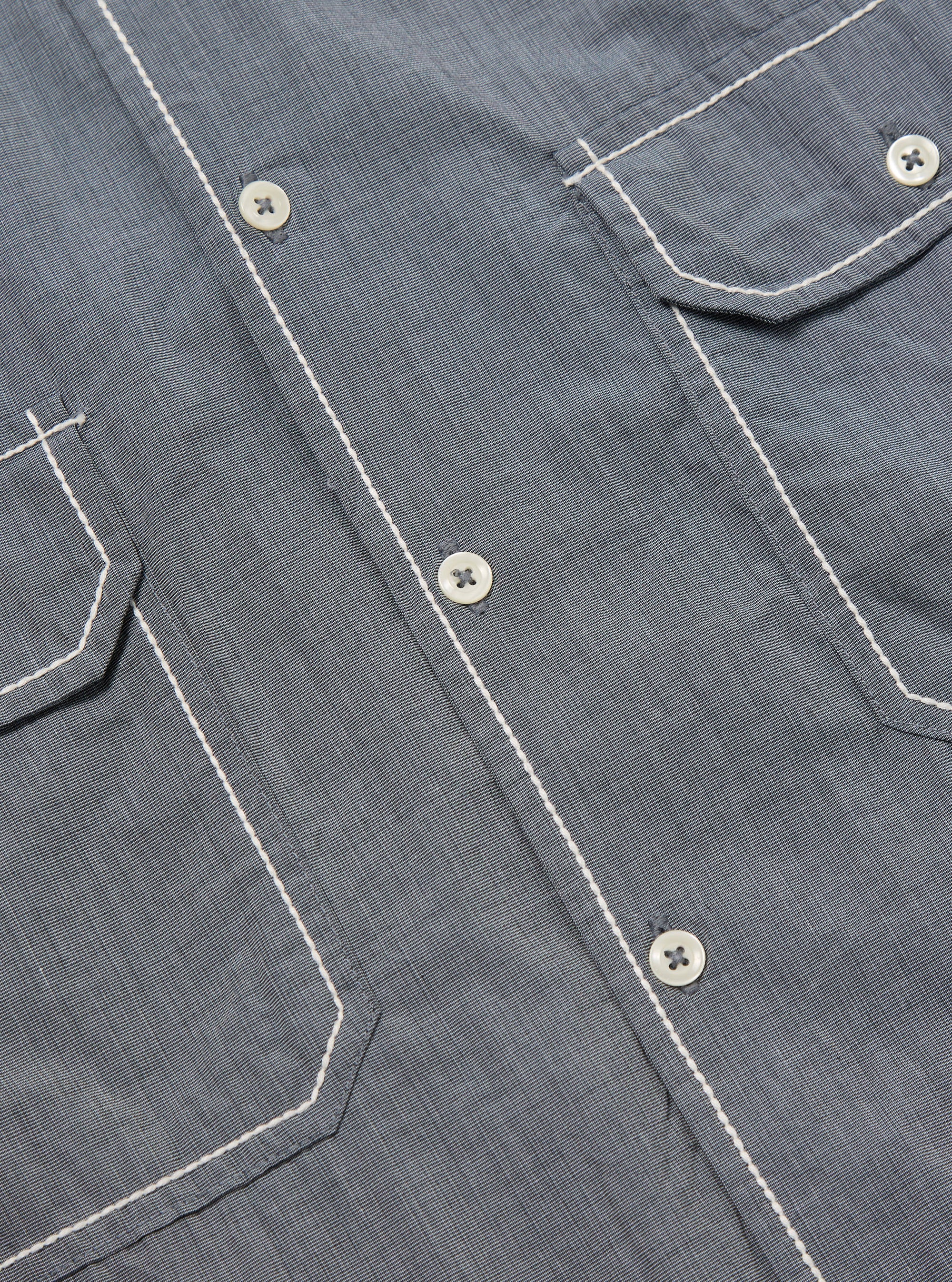 Close-up of the Grey End On End Cotton Utility SS Shirt. Shows the texture of the grey cotton, white buttons, and contrasting white stitching on the pockets and placket.
