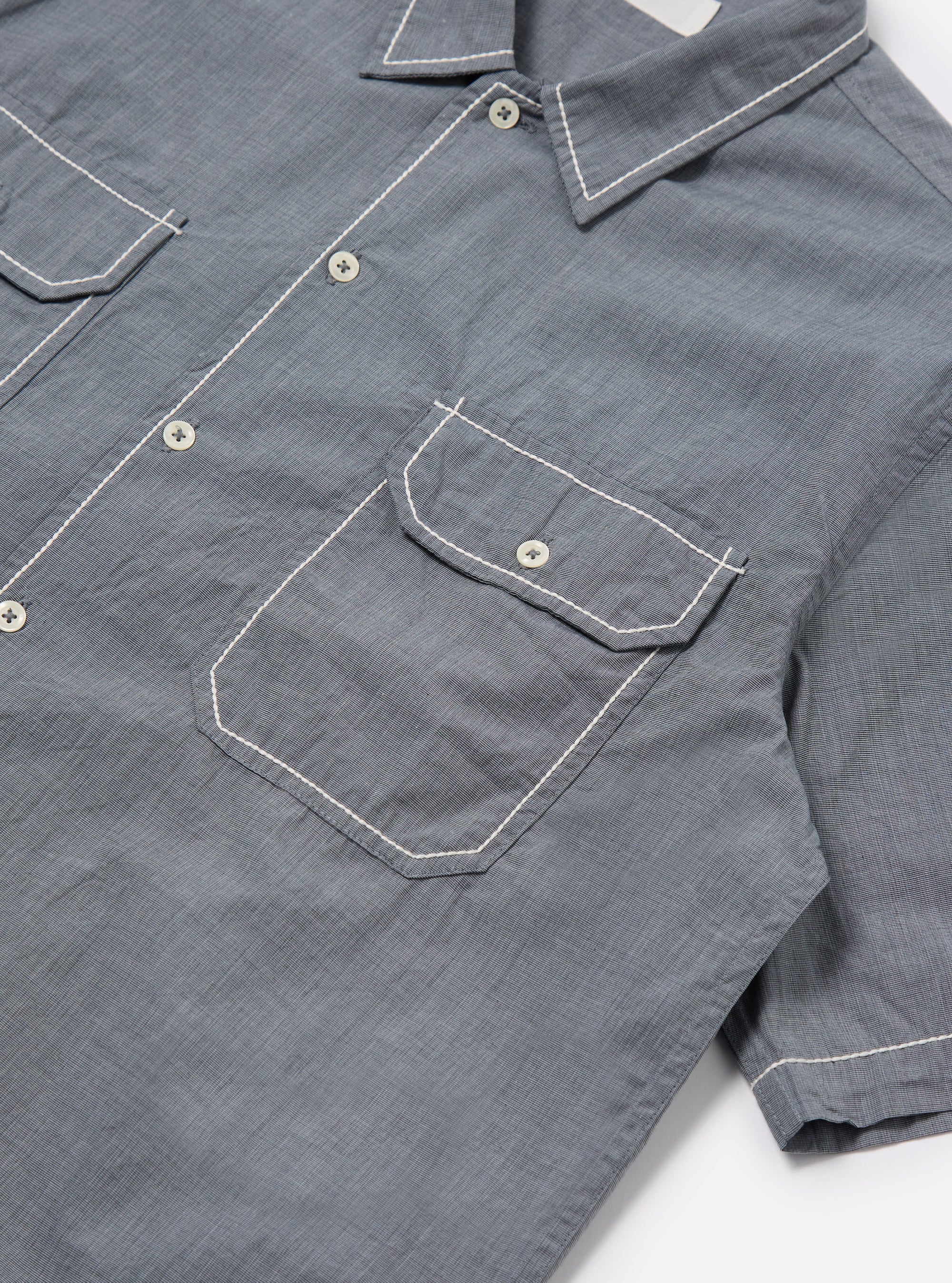 Close-up of the Grey End On End Cotton Utility SS Shirt on a white surface. The shirt features white stitching details on the pockets, collar, and sleeves.