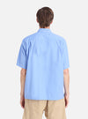 Back view of a model wearing the Blue End On End Cotton Utility SS Shirt. The light blue, cotton shirt is paired with tan shorts against a white background.