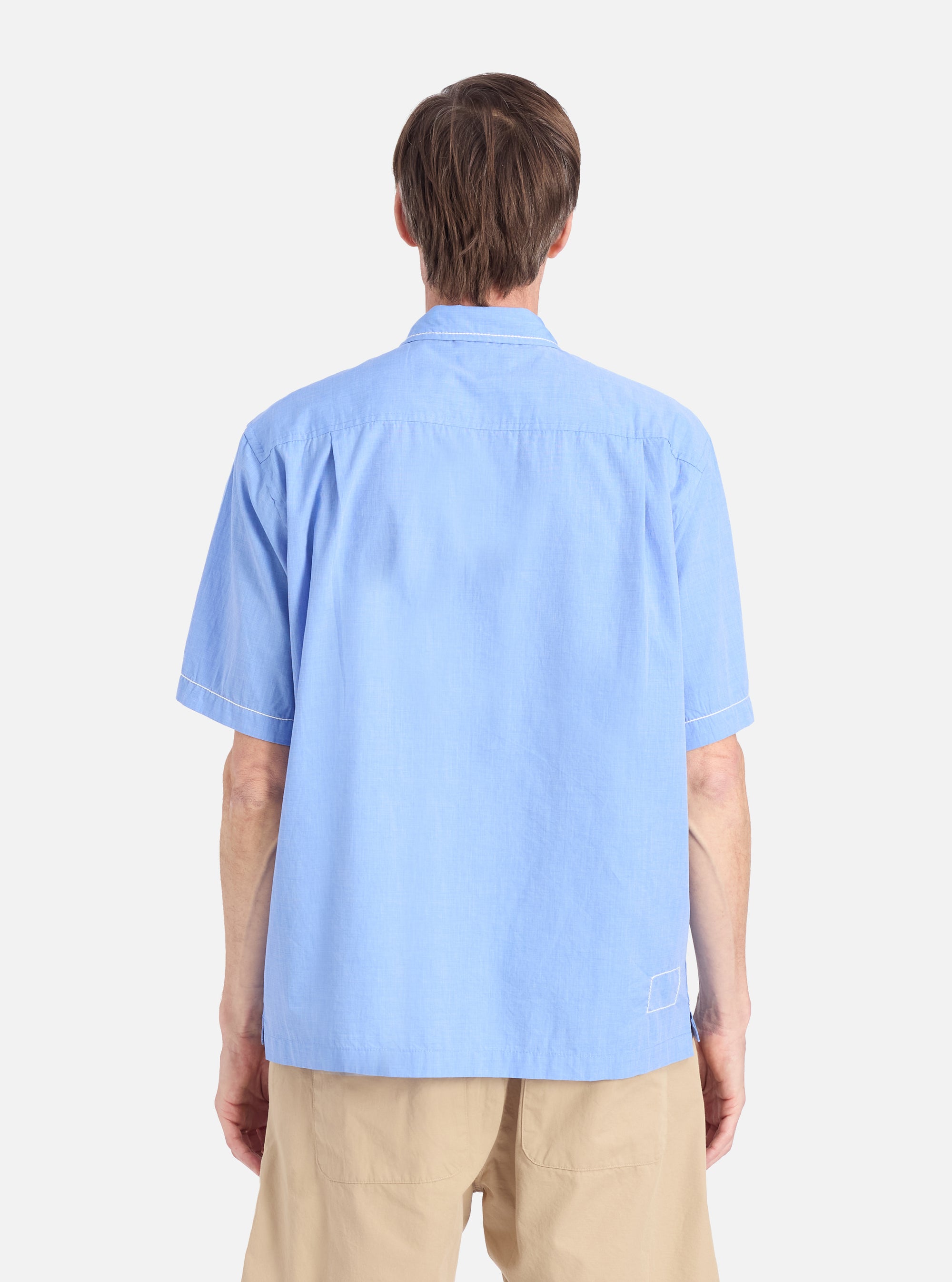 Back view of a model wearing the Blue End On End Cotton Utility SS Shirt. The light blue, cotton shirt is paired with tan shorts against a white background.
