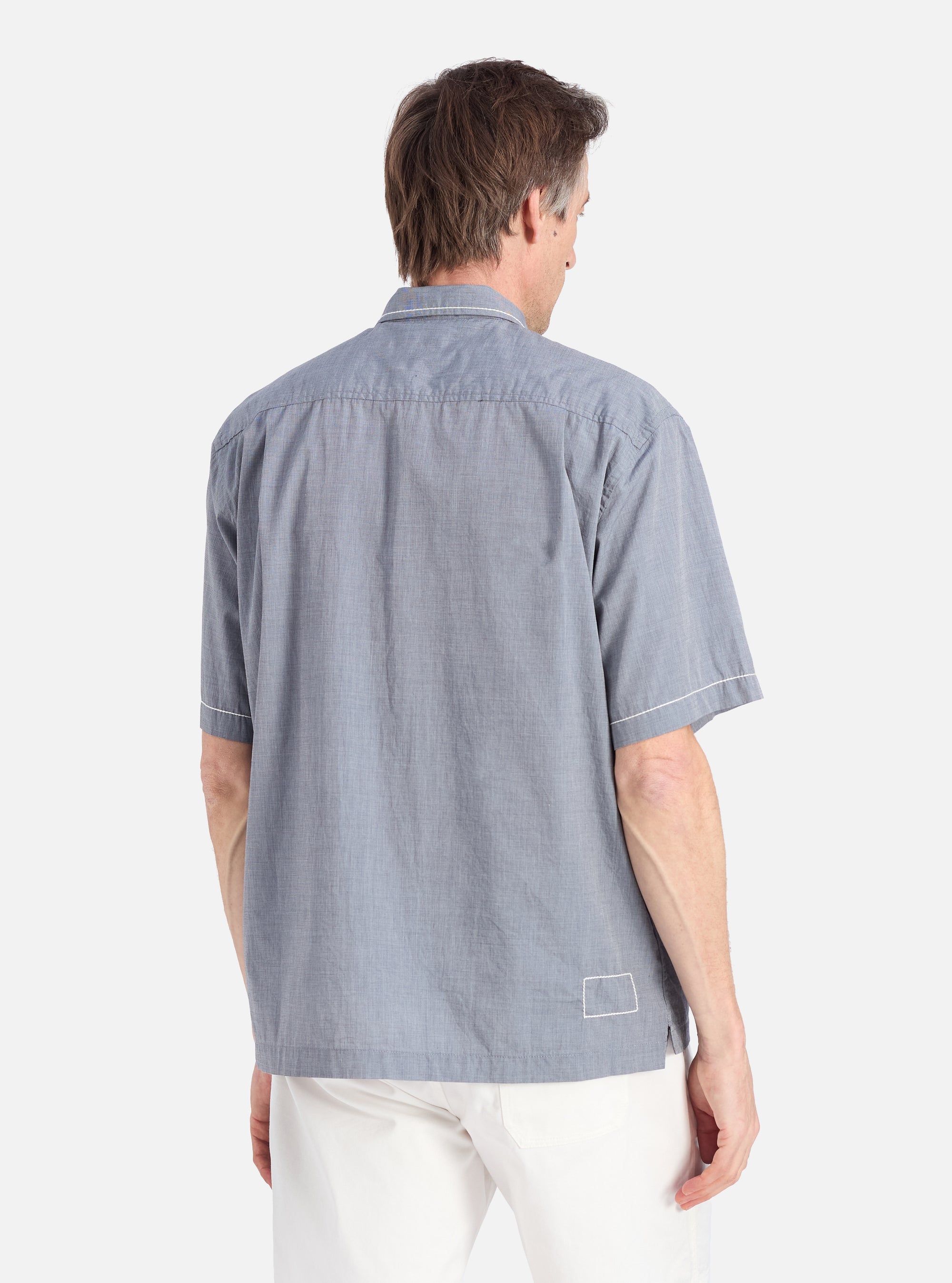 A man stands against a white backdrop, showcasing the back of the Grey End On End Cotton Utility SS Shirt. The shirt is paired with white pants.