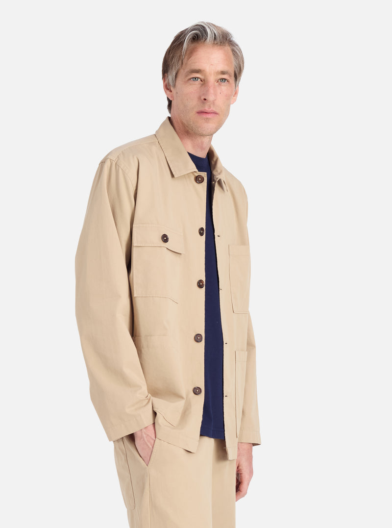 A model poses in a Sand Military Cotton Dockside Overshirt. The sand-colored cotton overshirt is displayed against a white background.