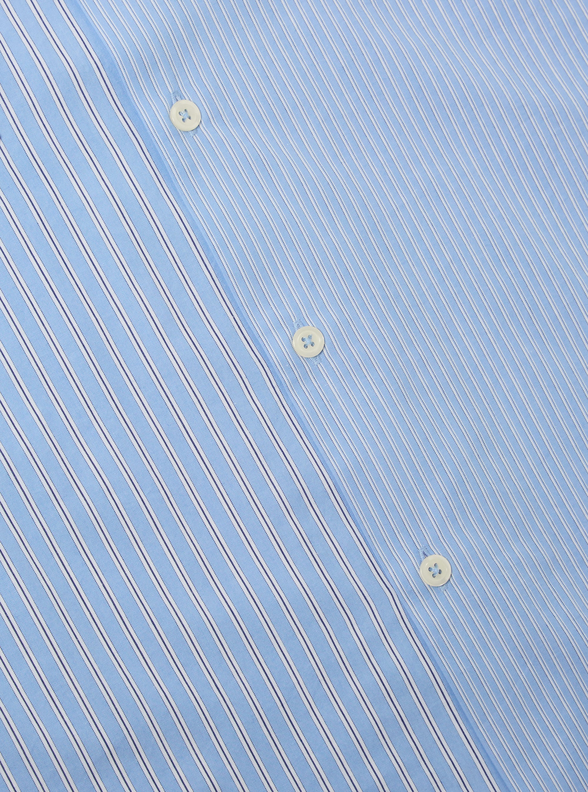 Close-up of the Blue Vila Stripes Sal Road Shirt, showcasing its light blue fabric with white and navy stripes and button details. The shirt is laid flat on a neutral surface.