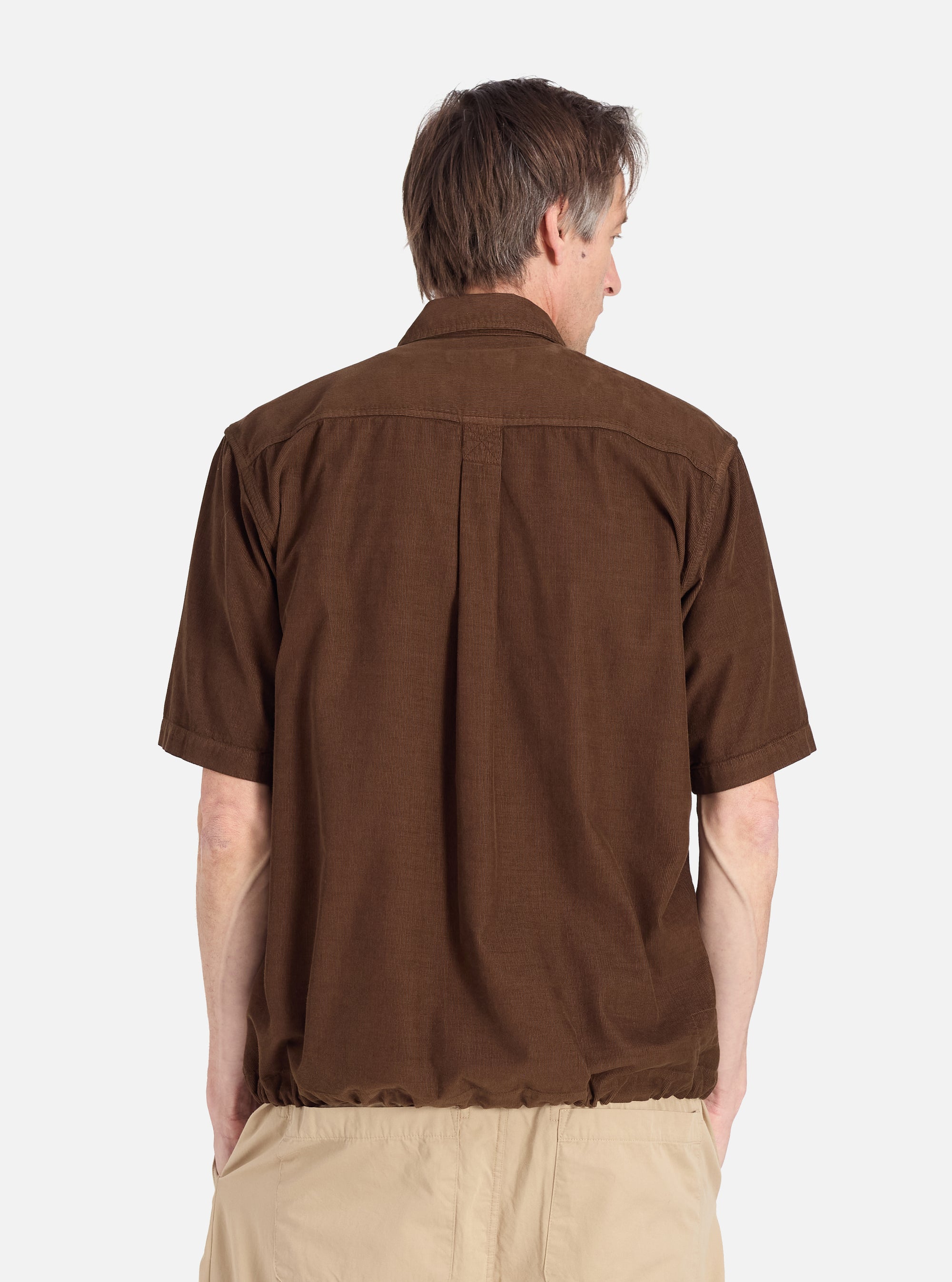 Back view of a man wearing the Khaki Summer Cord Tech Overshirt in brown corduroy with khaki pants, against a white background. The overshirt has short sleeves and a relaxed fit.