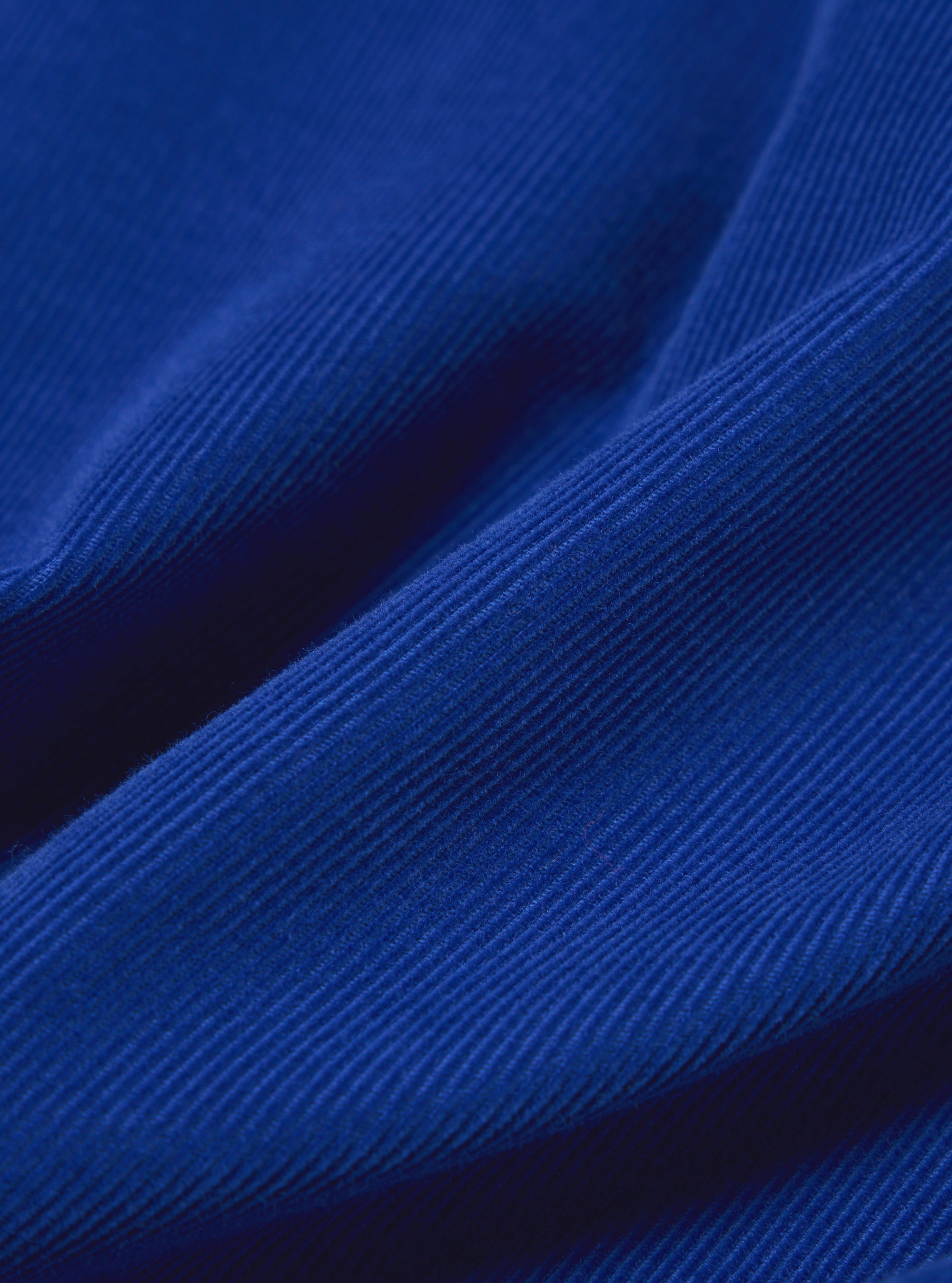 Close-up of the Work Blue Summer Cord Tech Overshirt fabric. The rich blue corduroy texture is highlighted with soft lighting, showing the material's fine ridges.