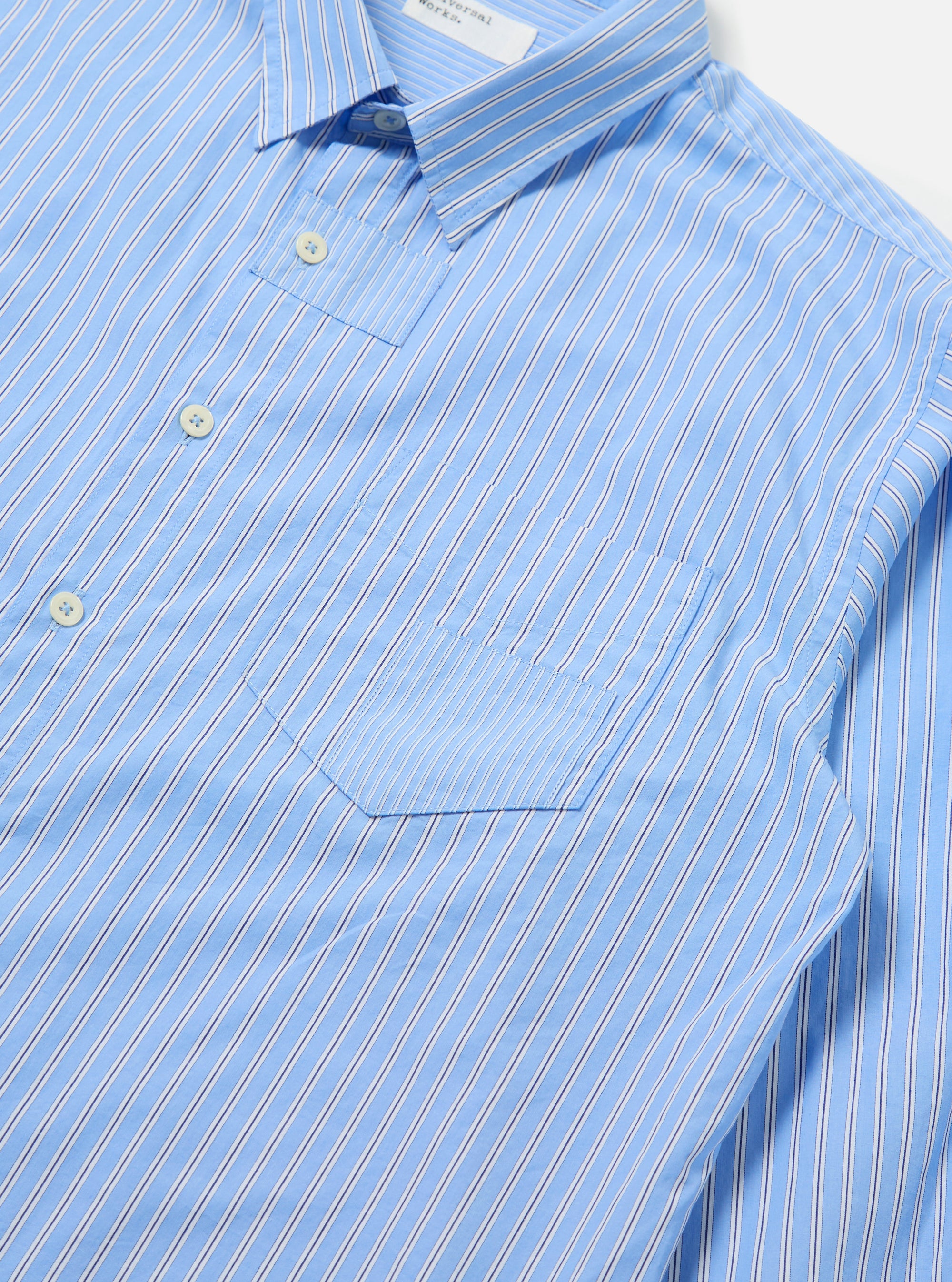 Close-up of the Blue Vila Stripes Patched Shirt on a white surface. The shirt features light blue and white stripes with a patched pocket.