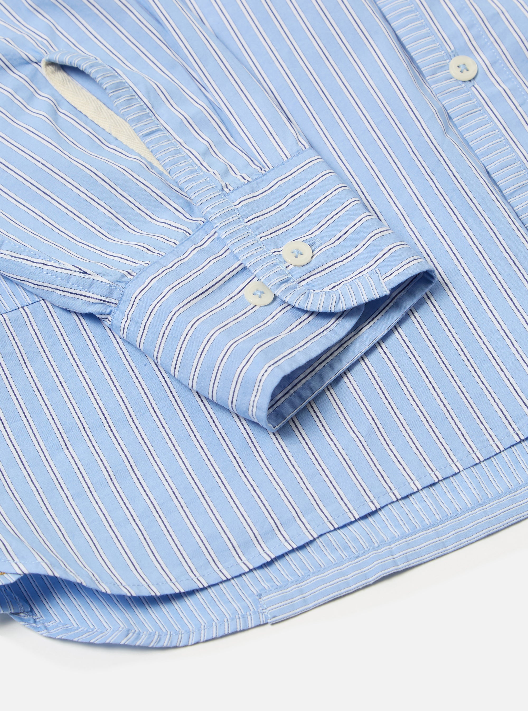 Close-up of the Blue Vila Stripes Patched Shirt on a white surface. Features blue and white stripes, buttoned cuffs, and a crisp, tailored fit.