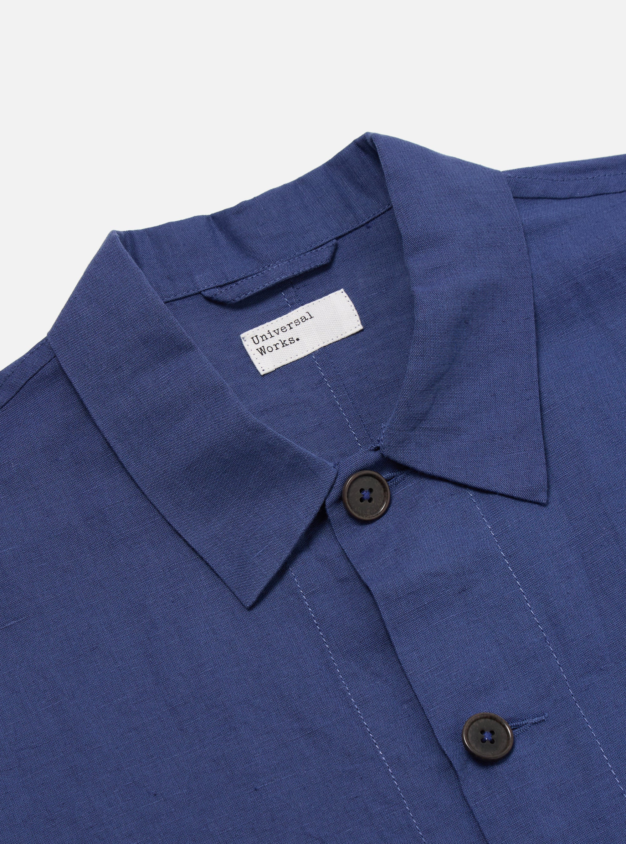 Close-up of the Blue Linen Cotton Shirting Travail Overshirt on a white background. The blue linen cotton blend is visible, along with the collar, buttons, and brand label.