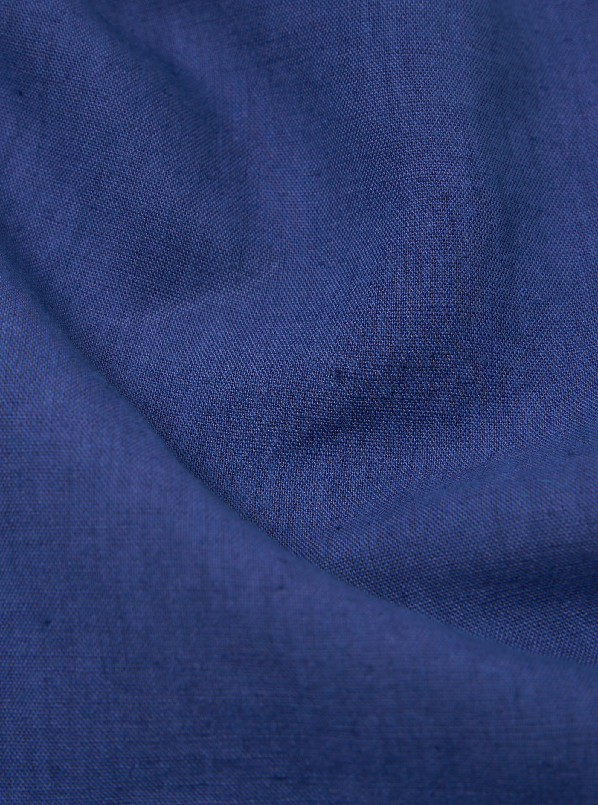 Close-up of the blue linen cotton shirting Travail Overshirt fabric. The material is draped to show texture and color. 
