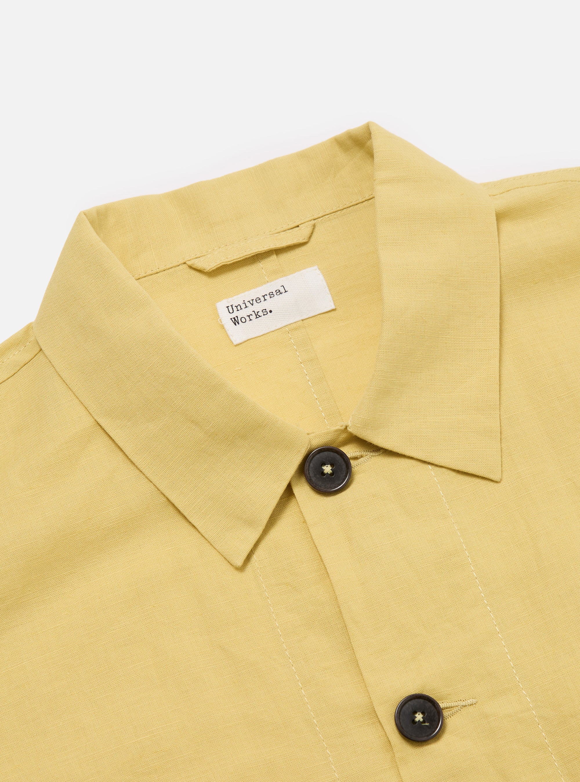 Close-up of the Lemon Linen Cotton Shirting Travail Overshirt on a white background. The light yellow overshirt has dark brown buttons and a visible brand label.
