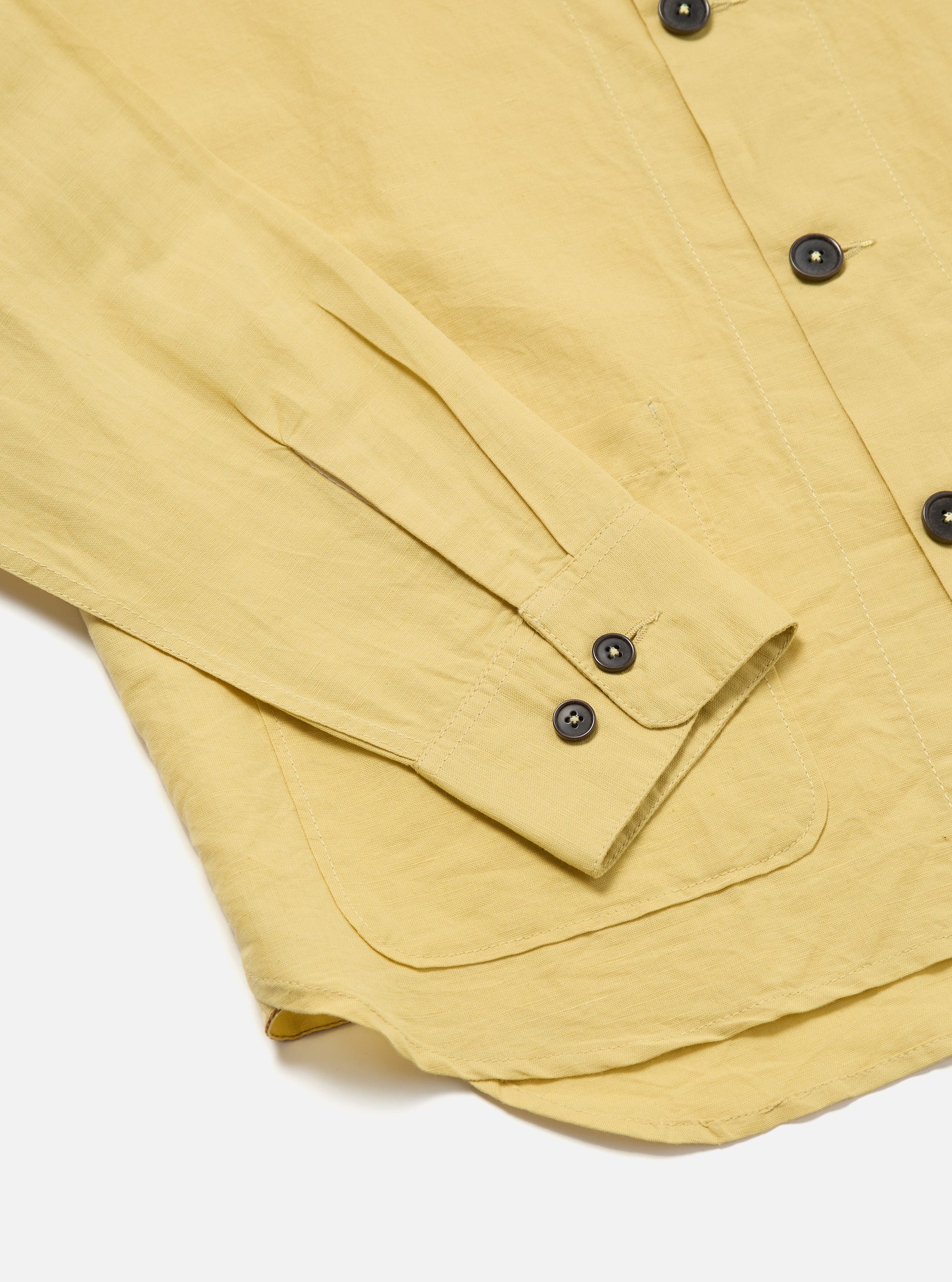 Close-up of the Lemon Linen Cotton Shirting Travail Overshirt on a white surface. Shows the sleeve, buttons, and pocket detail of the lemon-colored linen cotton shirt.