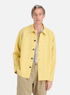 A model poses in a Lemon Linen Cotton Shirting Travail Overshirt. The lemon overshirt is paired with patterned pants. Shot in a studio on a white background.