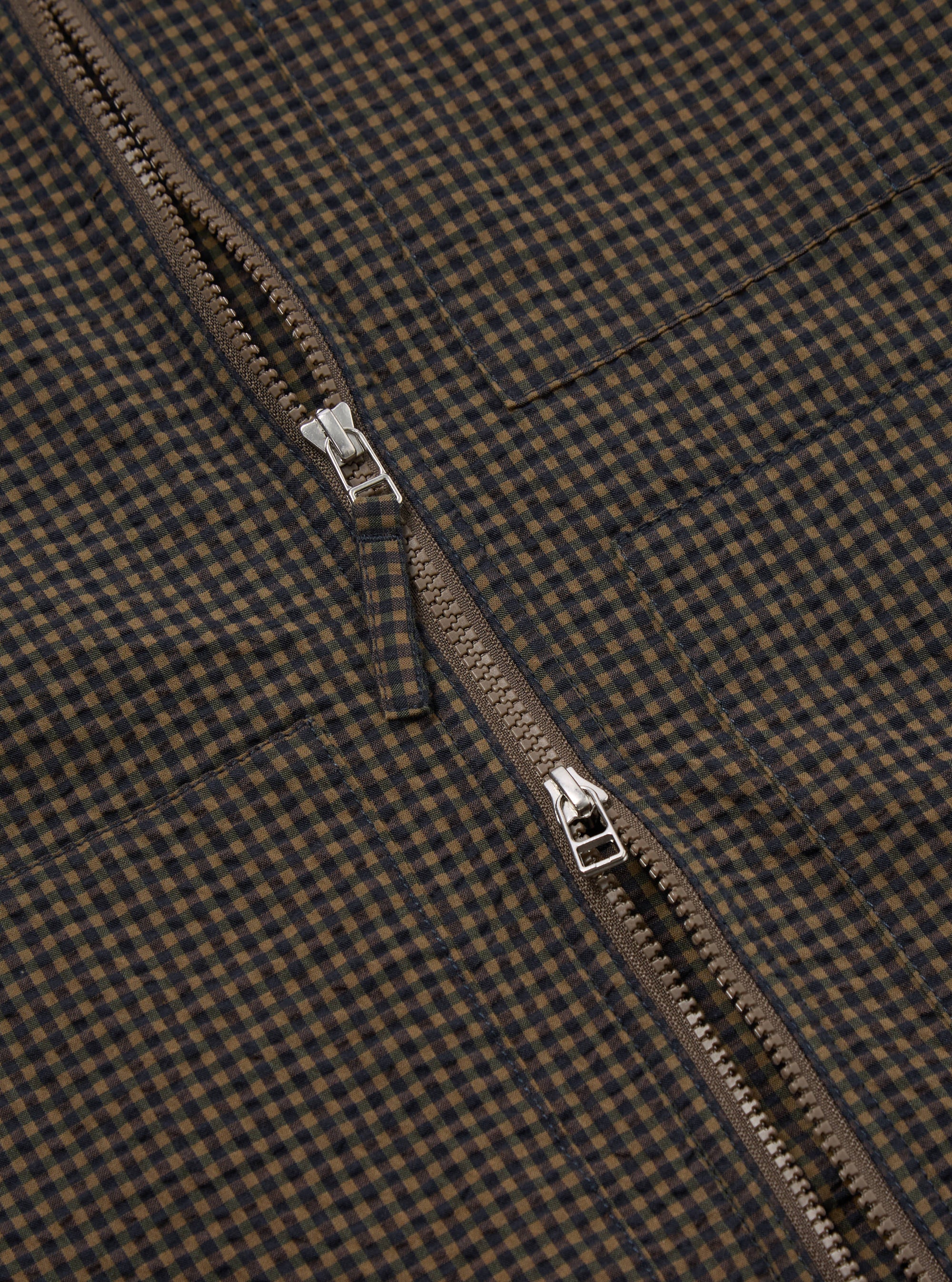 Close-up of the Navy Japanese Seersucker Zip Uniform Jacket showing the zipper and the navy and brown checkered seersucker fabric. The jacket is laid flat on a neutral surface.