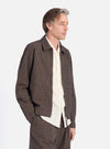 A man in profile on a white background wears the Navy Japanese Seersucker Zip Uniform Jacket. The jacket is brown and black check with a zip front. He wears a cream shirt underneath.