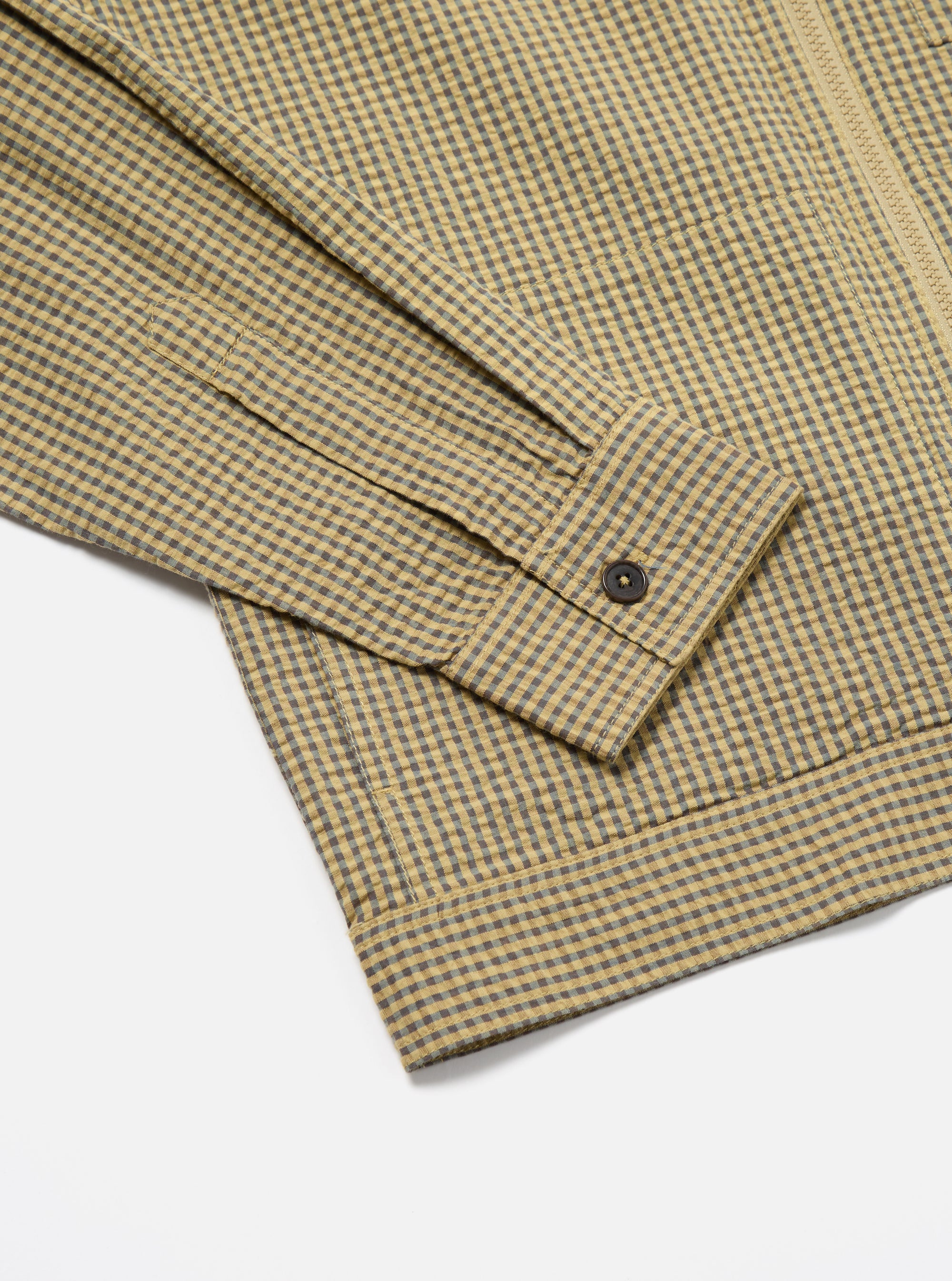 Close-up of the Yellow Japanese Seersucker Zip Uniform Jacket on a white surface. Shows the sleeve and hem, highlighting the yellow and gray checkered pattern and seersucker texture.
